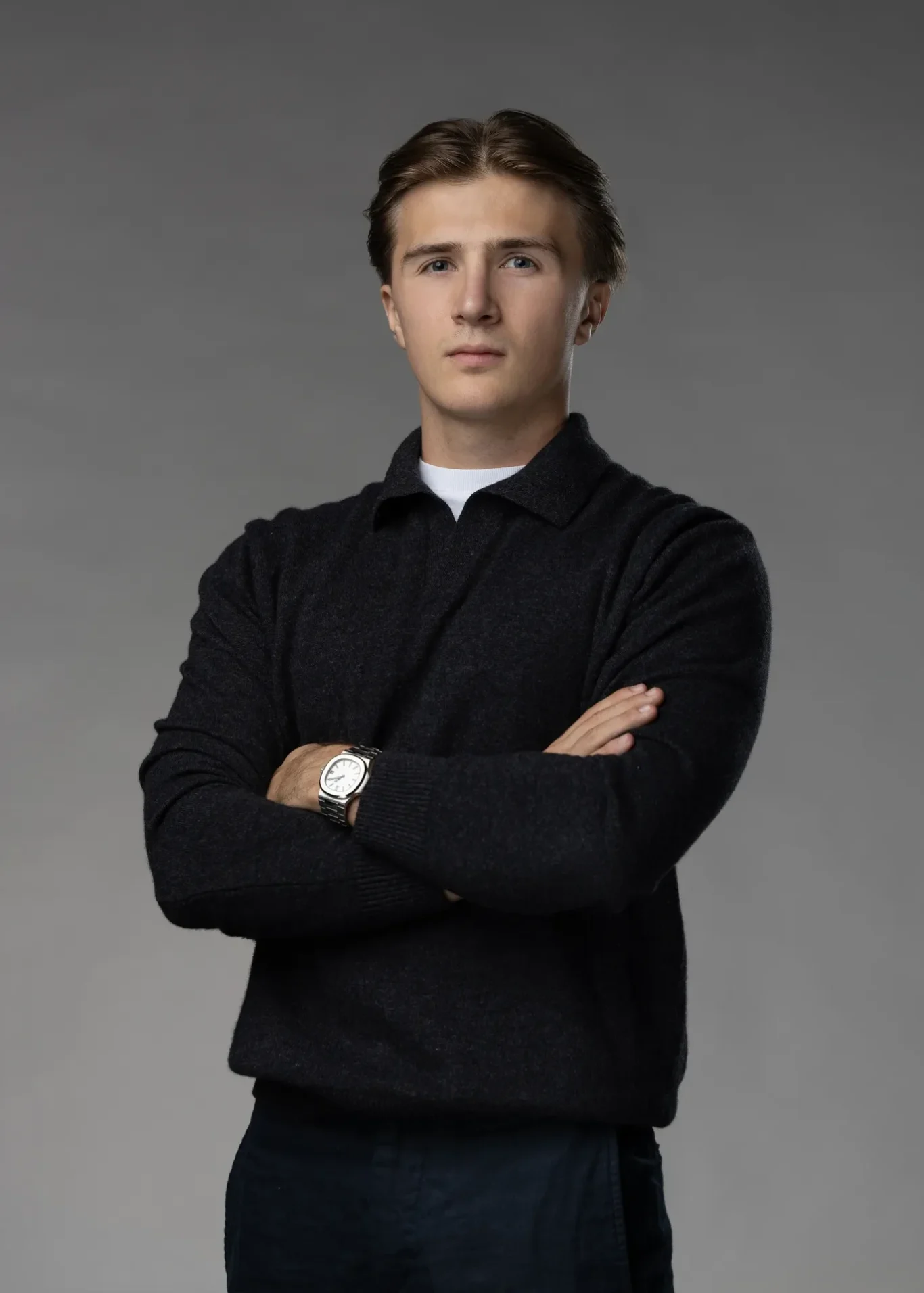 Entrepreneur standing with arms crossed in a black knit sweater against a dark grey studio backdrop. Editorial business portrait by MRPS in Dubai for a financial magazine feature.