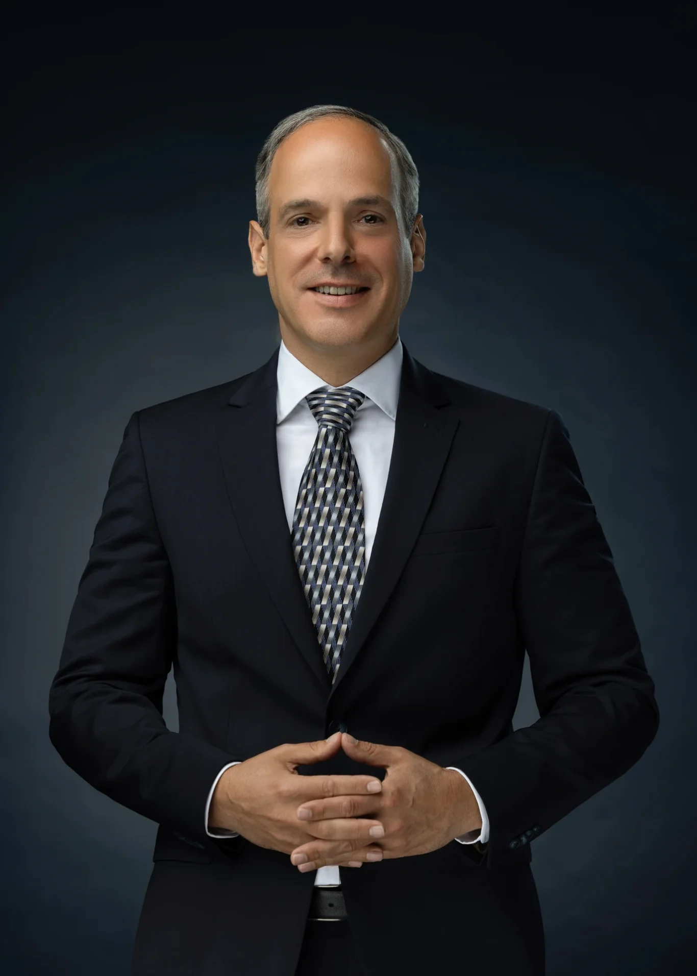 Standing executive portrait with hands together, navy suit and patterned tie. Corporate business portrait of a Dubai CEO, photographed at the MRPS studio in Business Bay.