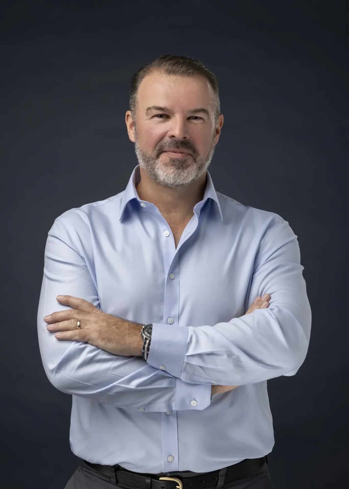 Rik Williams in a light blue shirt with sleeves rolled, arms crossed, dark navy backdrop. Corporate portrait photography by MRPS in Dubai, photographed by Nastaran.