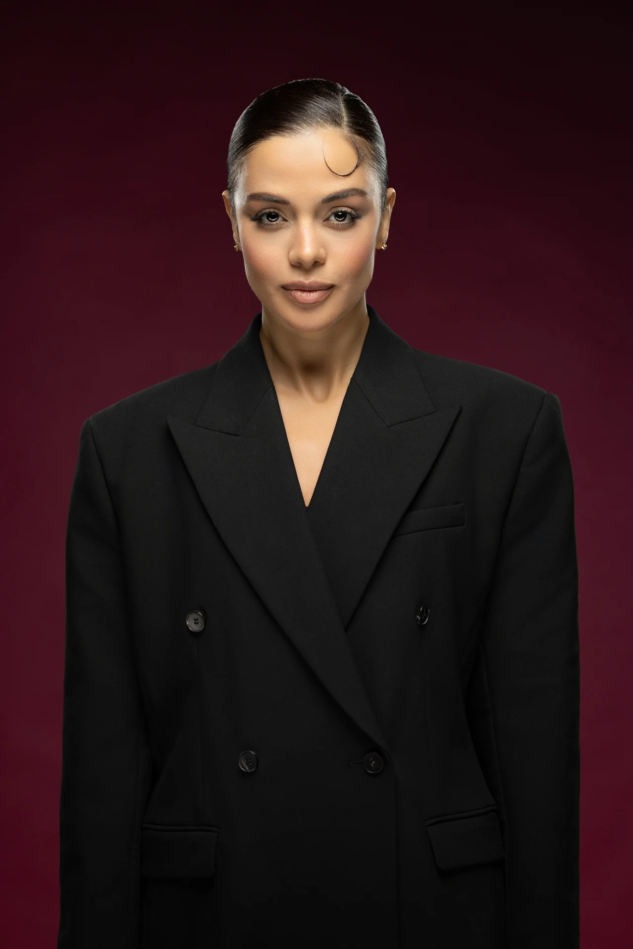 Front-facing LinkedIn headshot of a businesswoman in a black blazer against a deep burgundy studio backdrop.