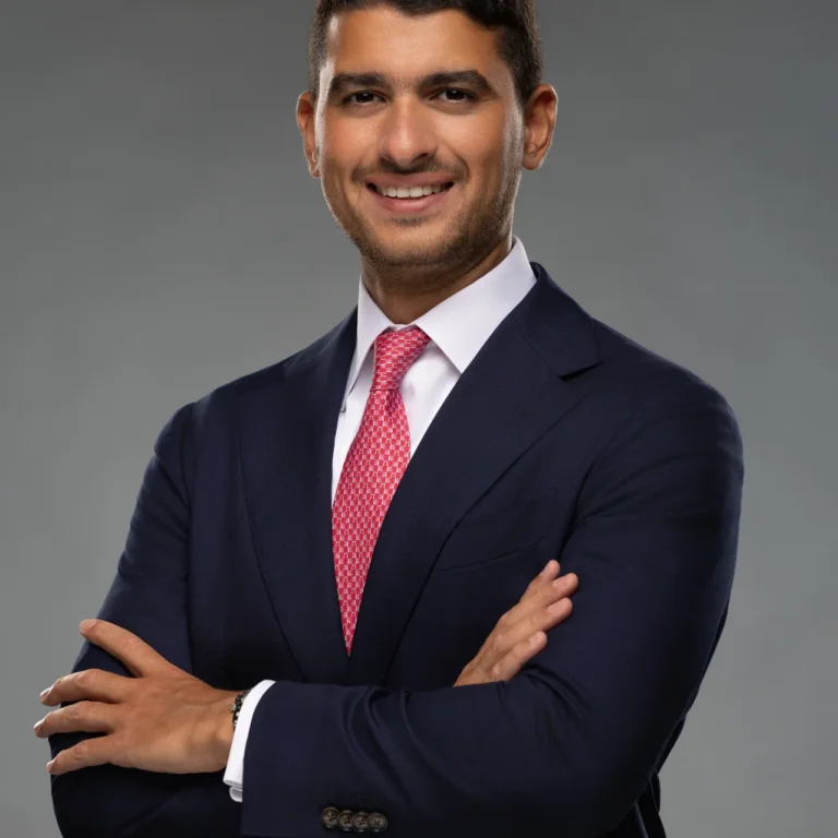 Smiling businessman in a navy suit and pink tie with arms crossed, a LinkedIn profile photo taken in a Dubai studio.