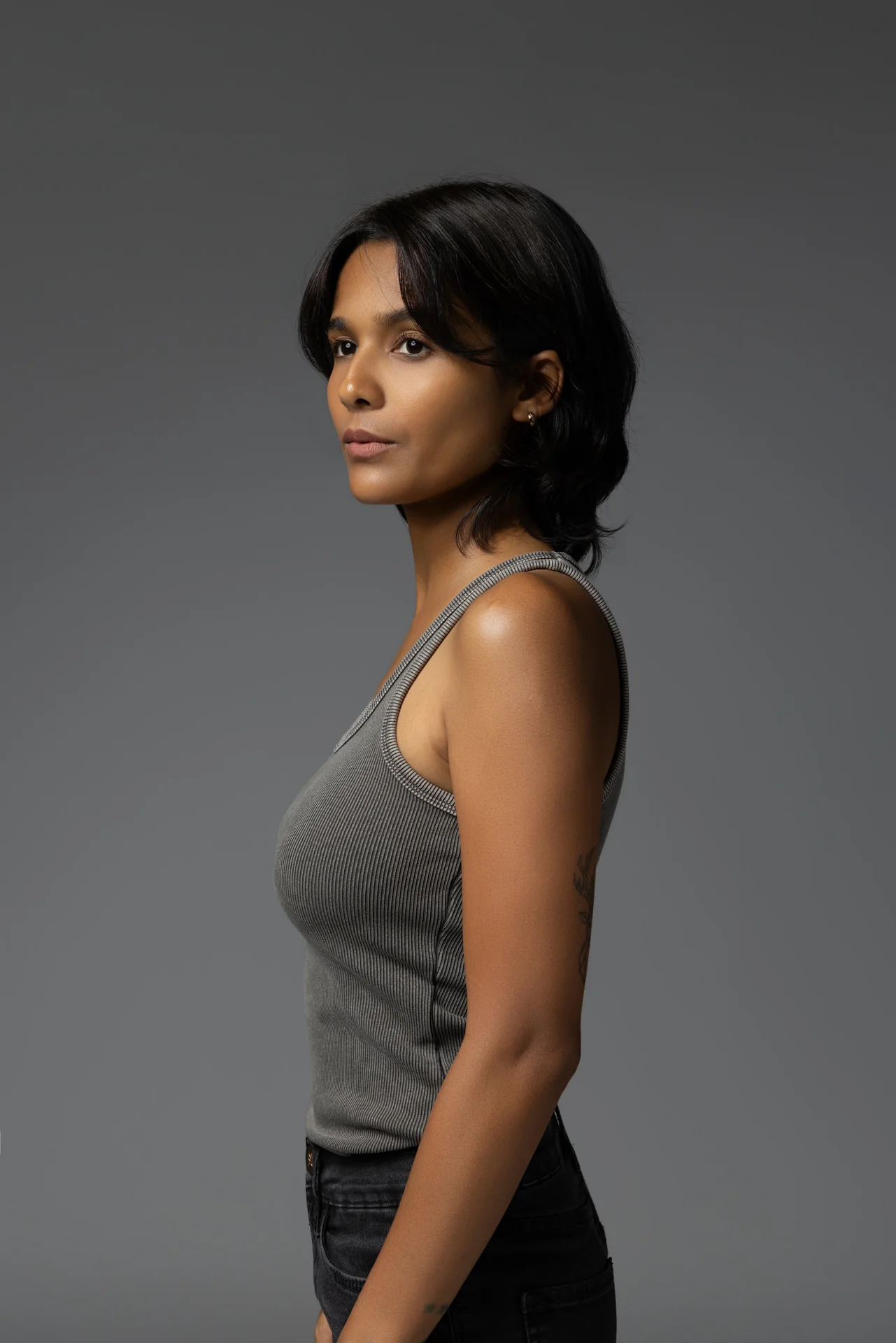 Side profile portrait of Mia in a grey tank top against a grey studio backdrop.