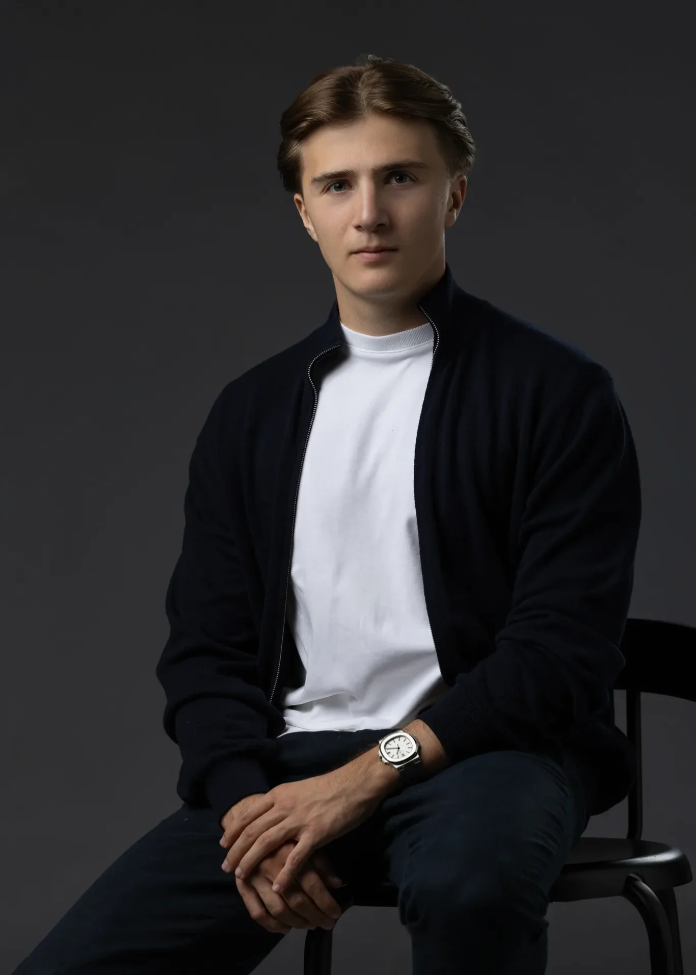 Entrepreneur seated and leaning forward with hands together, navy cardigan and white t-shirt. Editorial business portrait by MRPS in Dubai for a financial magazine feature.