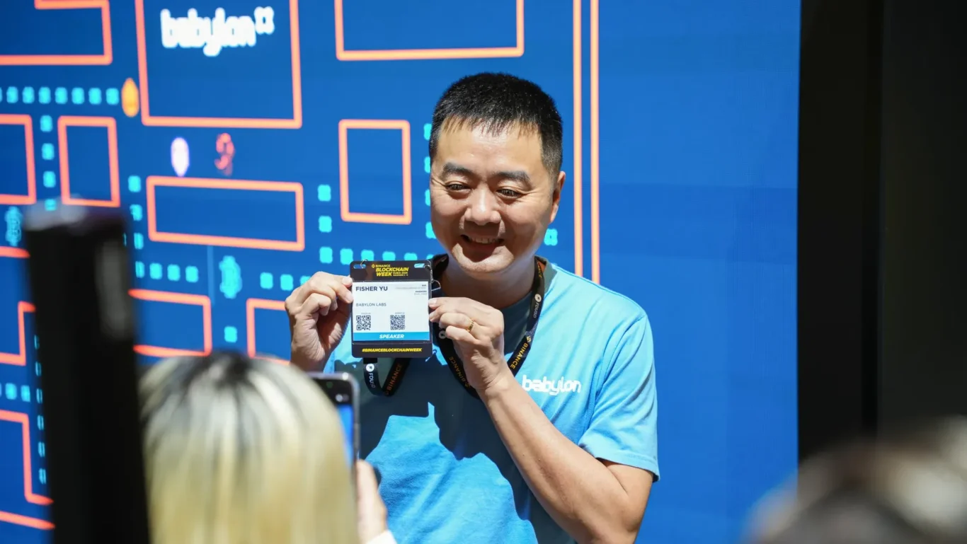 Babylon team member showing a visitor badge at the booth. Photographed by MRPS for Eventflare at Binance Blockchain Week 2025, Coca-Cola Arena, Dubai.
