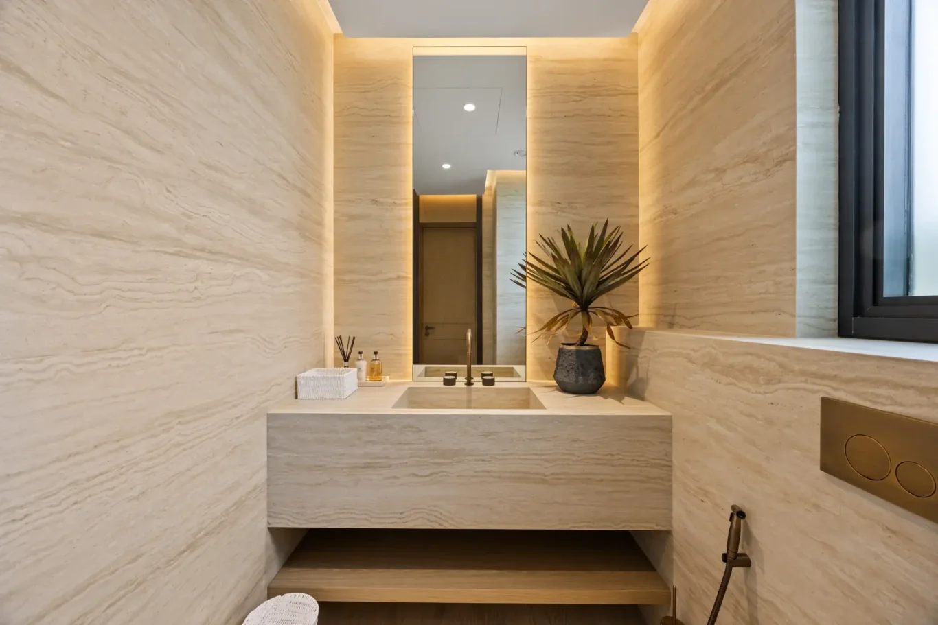Guest powder room with travertine walls and a backlit mirror, luxury villa in Jumeirah Islands, Dubai.