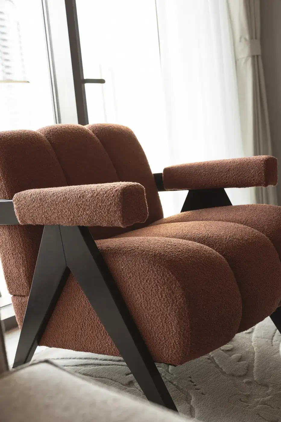 Rust boucle armchair with dark wooden frame in the living room. Interior design photography for Aziza Home by MRPS in Dubai.