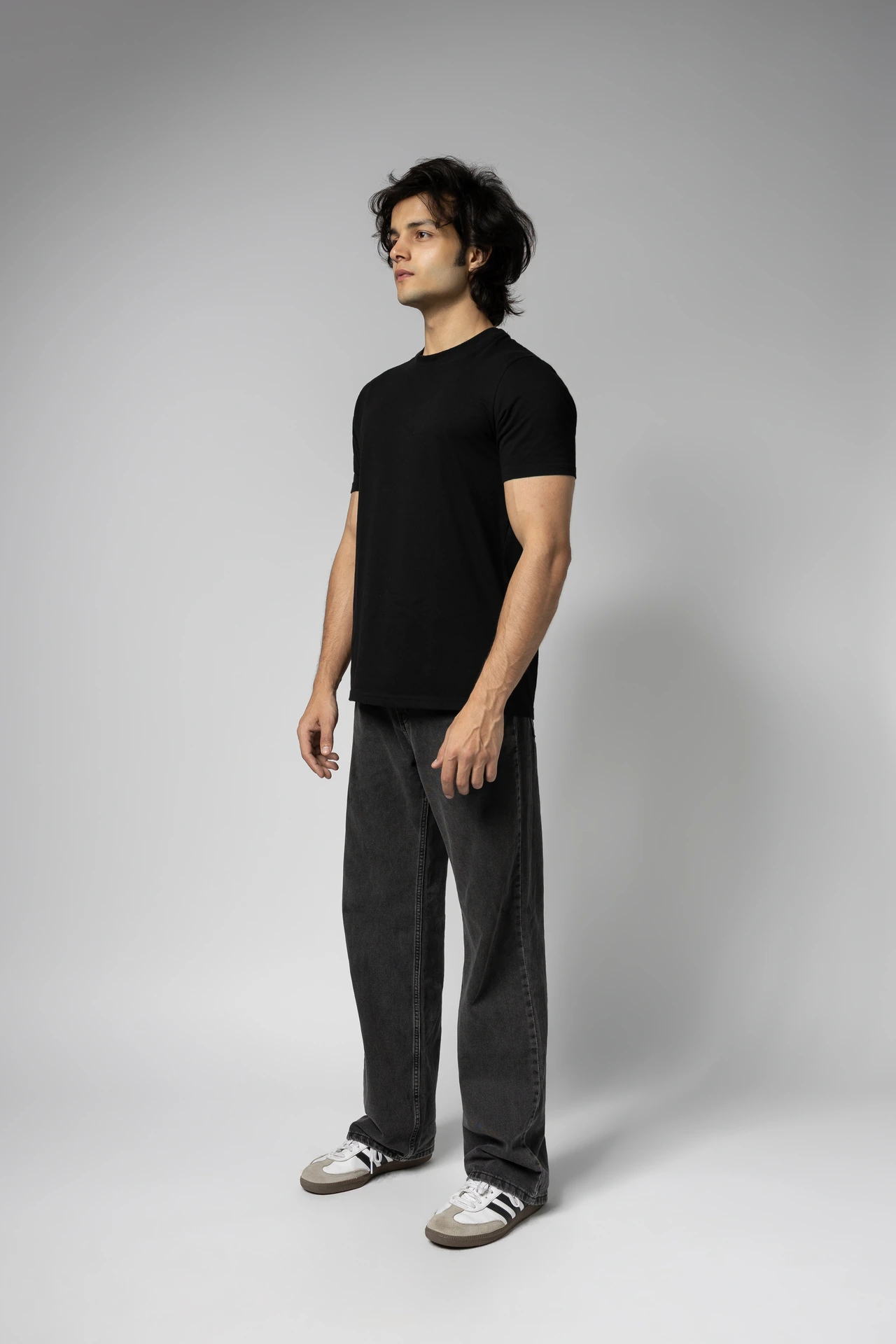 Full-length three-quarter view of Arsh in a black t-shirt and wide dark jeans, a studio digital.