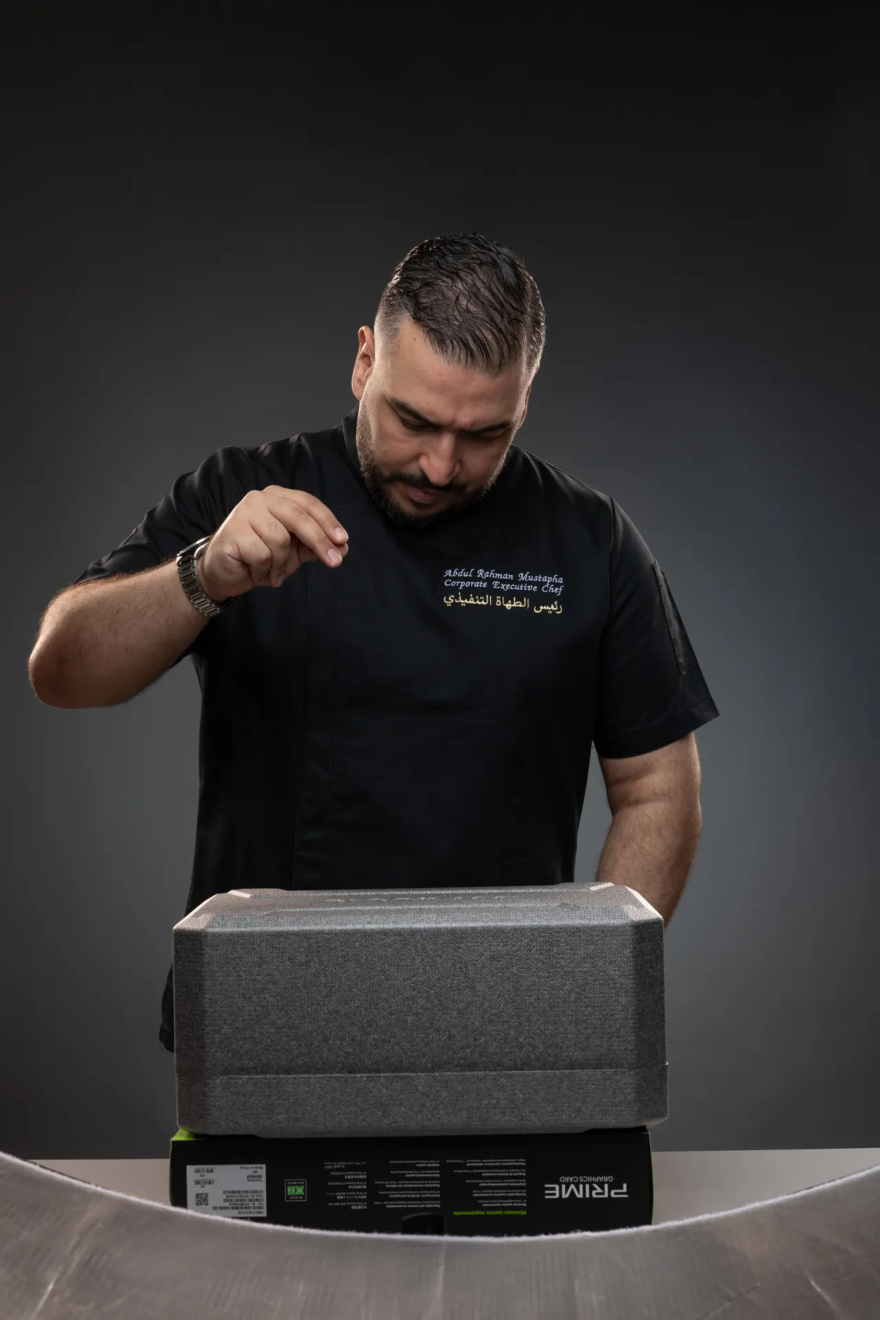 Studio reference photo of the chef making a salt-sprinkling gesture over a stand-in box, shot before the AI stage.