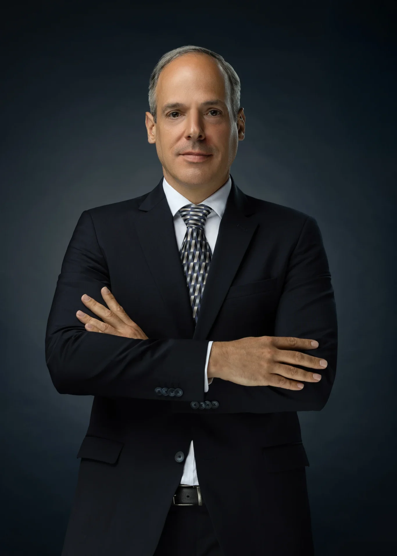 Three-quarter length portrait with arms crossed on a dark blue backdrop. Corporate business portrait of a Dubai CEO, photographed at the MRPS studio in Business Bay.