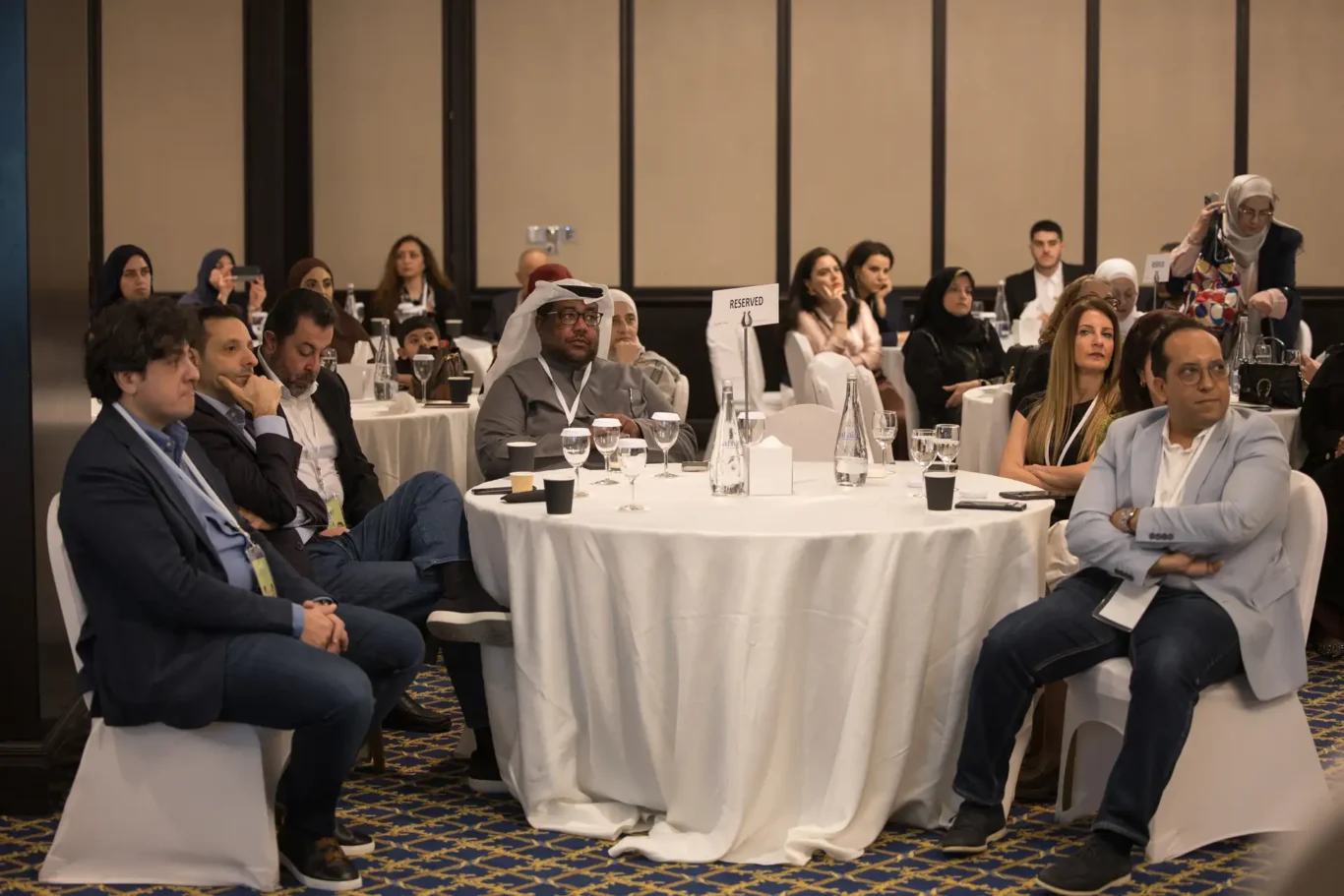 Guests seated at white round tables listening to a session in the ballroom. Corporate event photography by MRPS for My Arabic Publishing at Movenpick Grand Al Bustan, Dubai.
