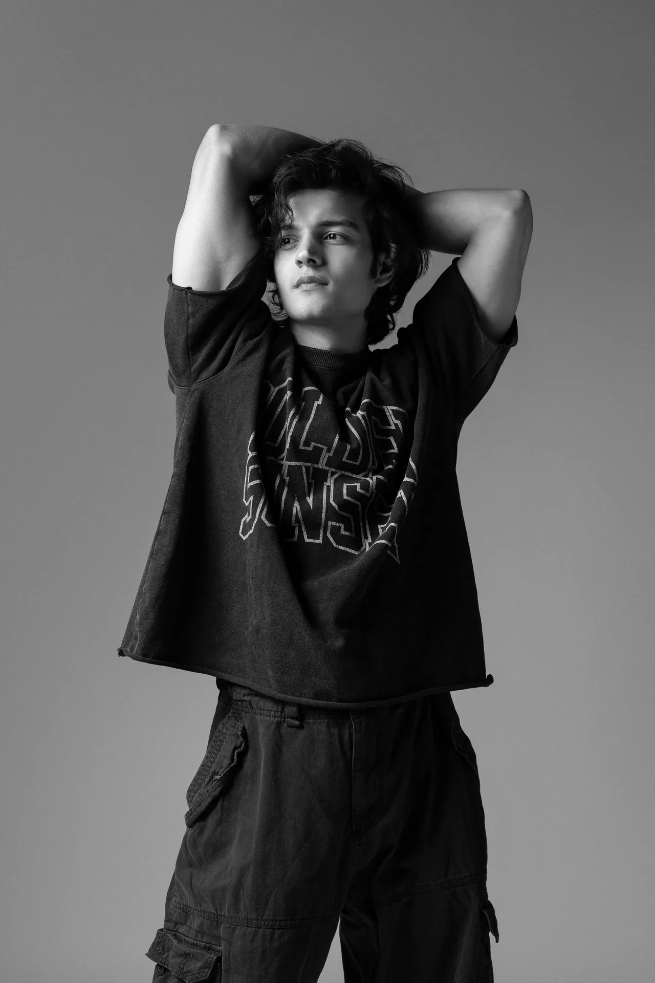 Black and white portrait of Arsh in an oversized graphic t-shirt with both arms raised behind his head.
