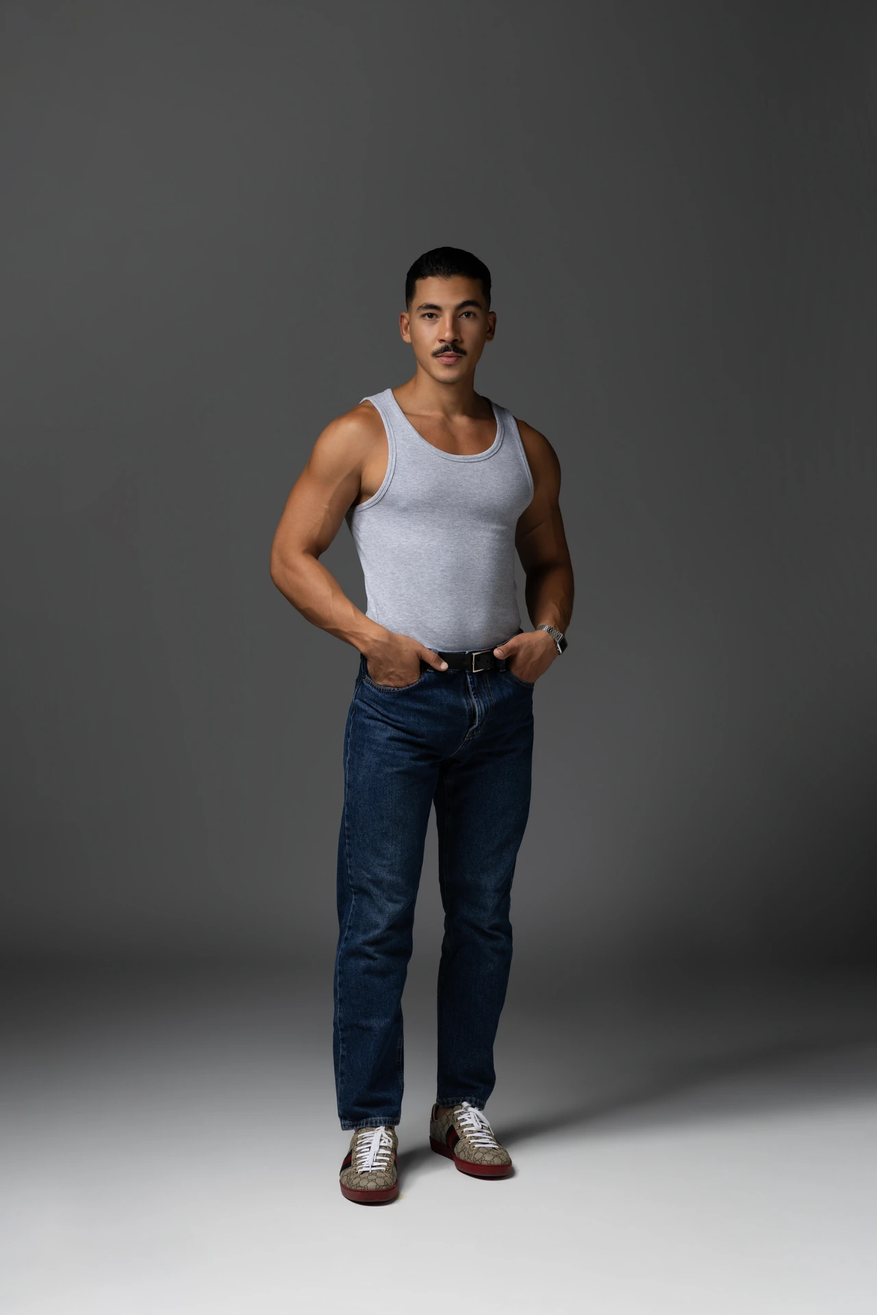 Full length digital in a white tank top and blue jeans, standing straight on a grey backdrop. Male modeling portfolio photoshoot by MRPS in Dubai, photographed by Nastaran.