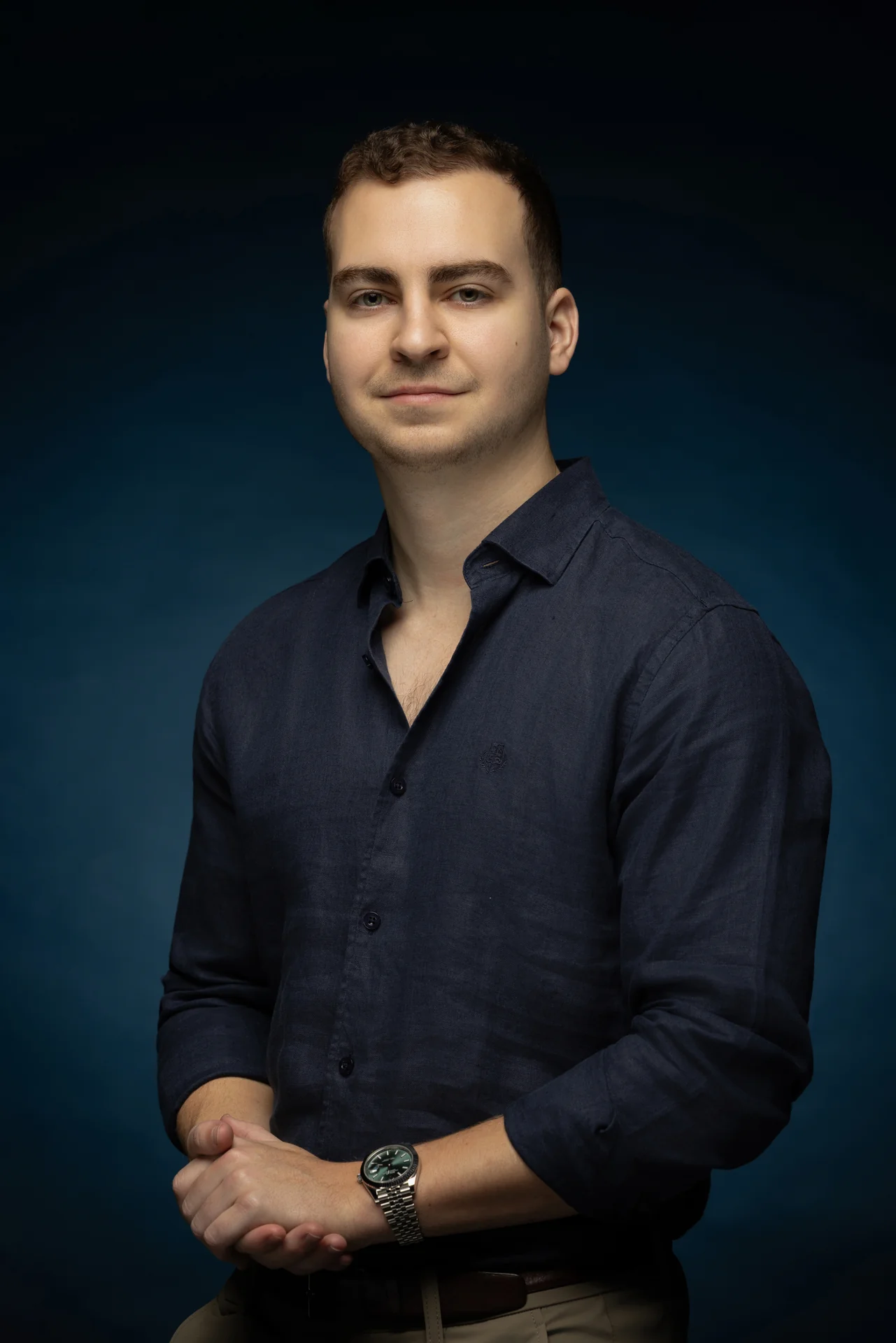 Seated portrait in a navy shirt with hands together on a blue backdrop. Professional headshot of Tim Ruscica of Tech With Tim, photographed at the MRPS studio in Dubai.