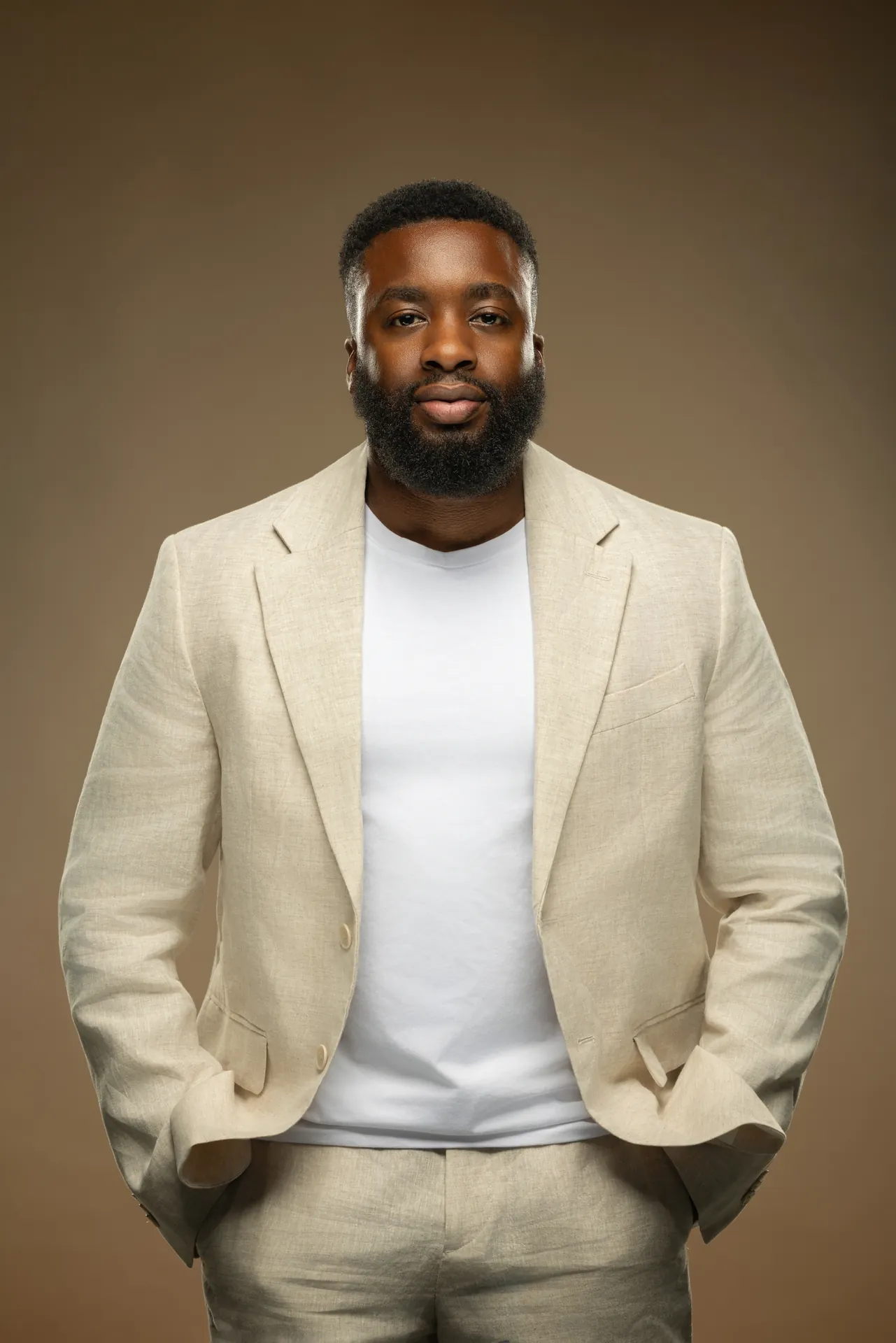 Personal branding portrait of a business owner in a cream linen suit and white t-shirt on a warm beige backdrop.