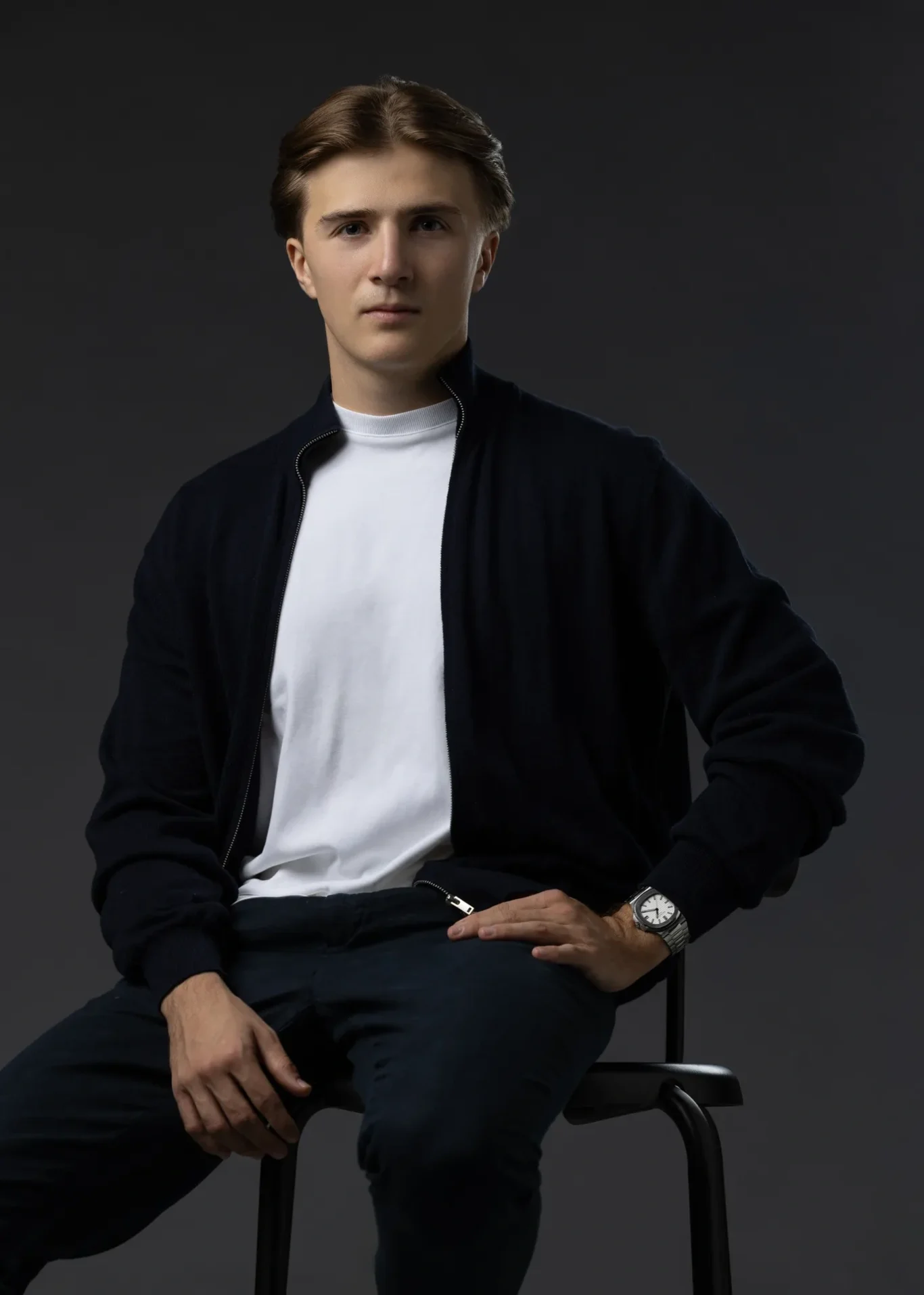 Seated portrait with hands on the knees, navy cardigan and white t-shirt, soft side light. Editorial business portrait by MRPS in Dubai for a financial magazine feature.