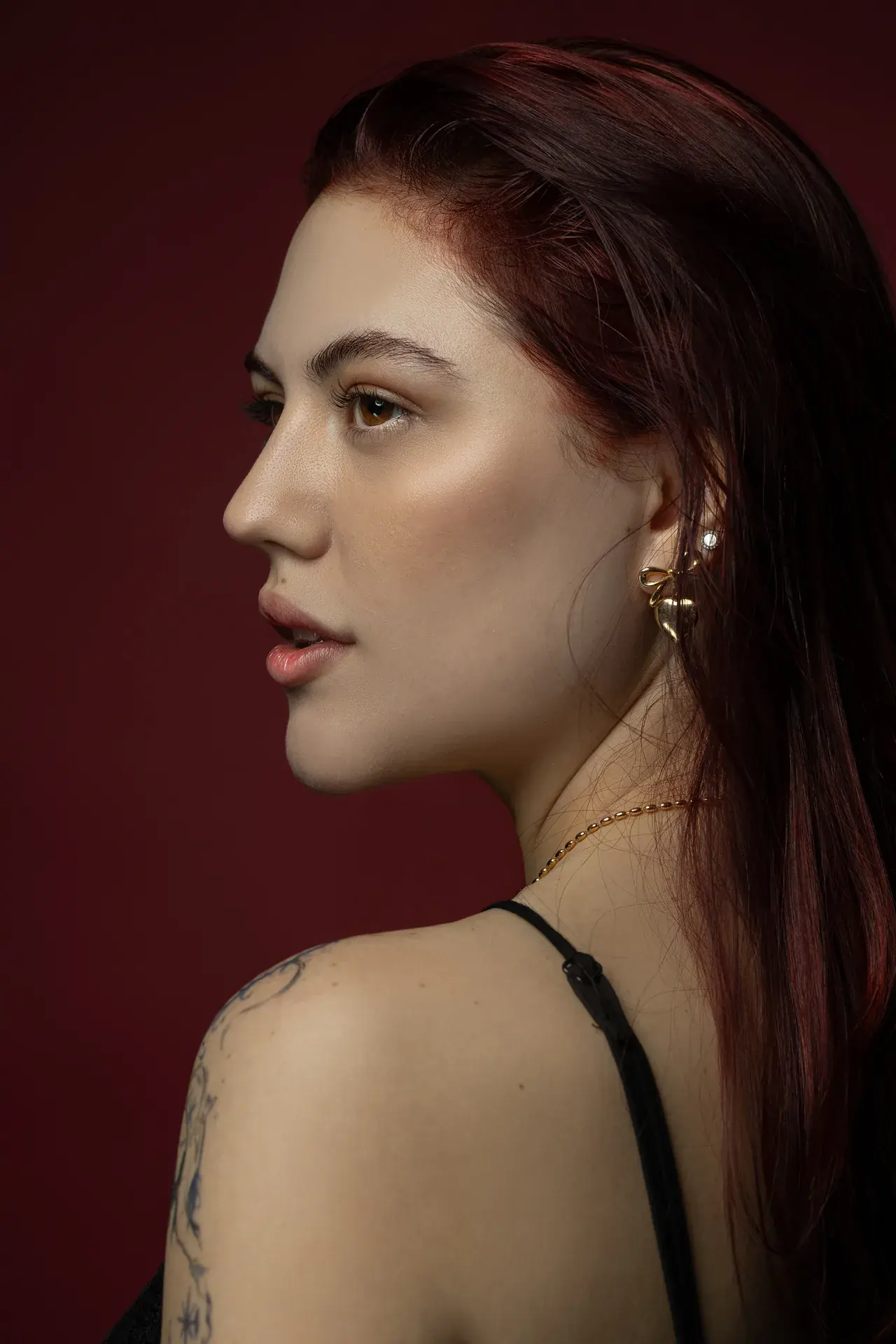 Clean side profile against the burgundy backdrop. Beauty portrait of model Julian, photographed by Nastaran at the MRPS studio in Dubai.