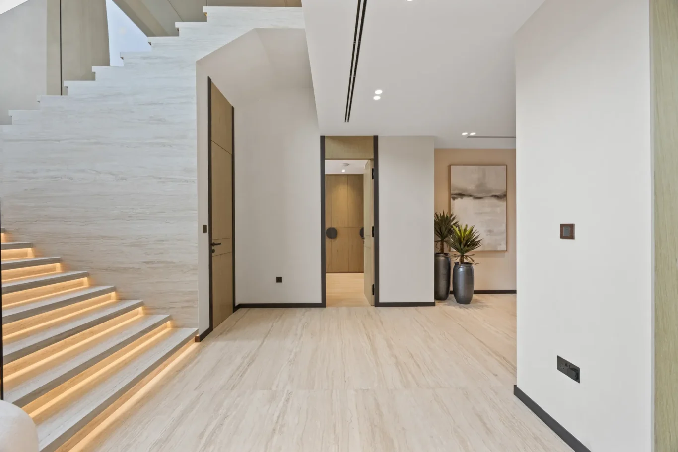 Travertine staircase with lit steps and the ground floor hallway, luxury villa in Jumeirah Islands, Dubai.