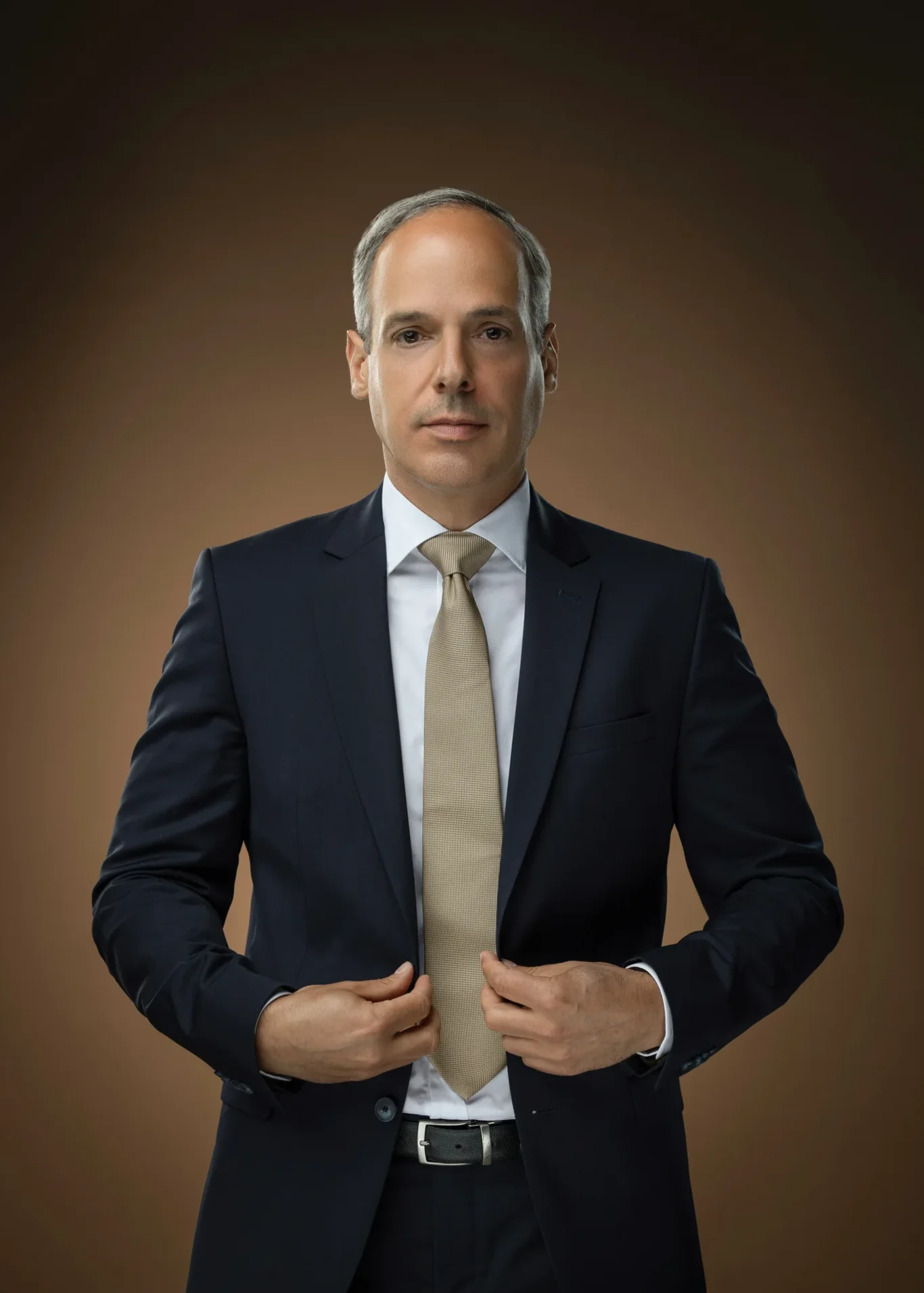 Executive buttoning his jacket against a warm brown backdrop. Corporate business portrait of a Dubai CEO, photographed at the MRPS studio in Business Bay.