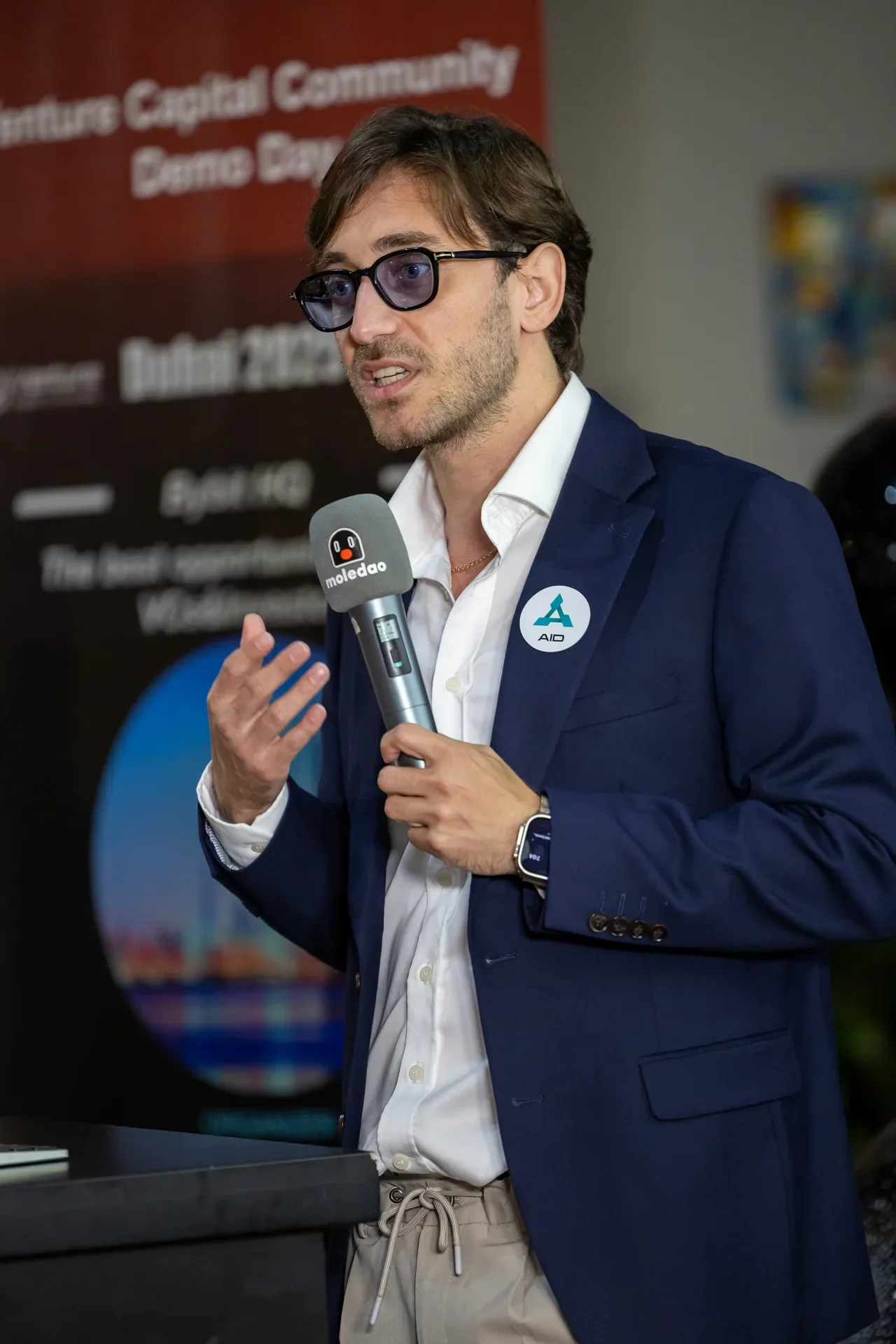 AID founder speaking with a microphone at a side event. Event photography by MRPS at Blockchain Life 2025, Festival Arena, Dubai.