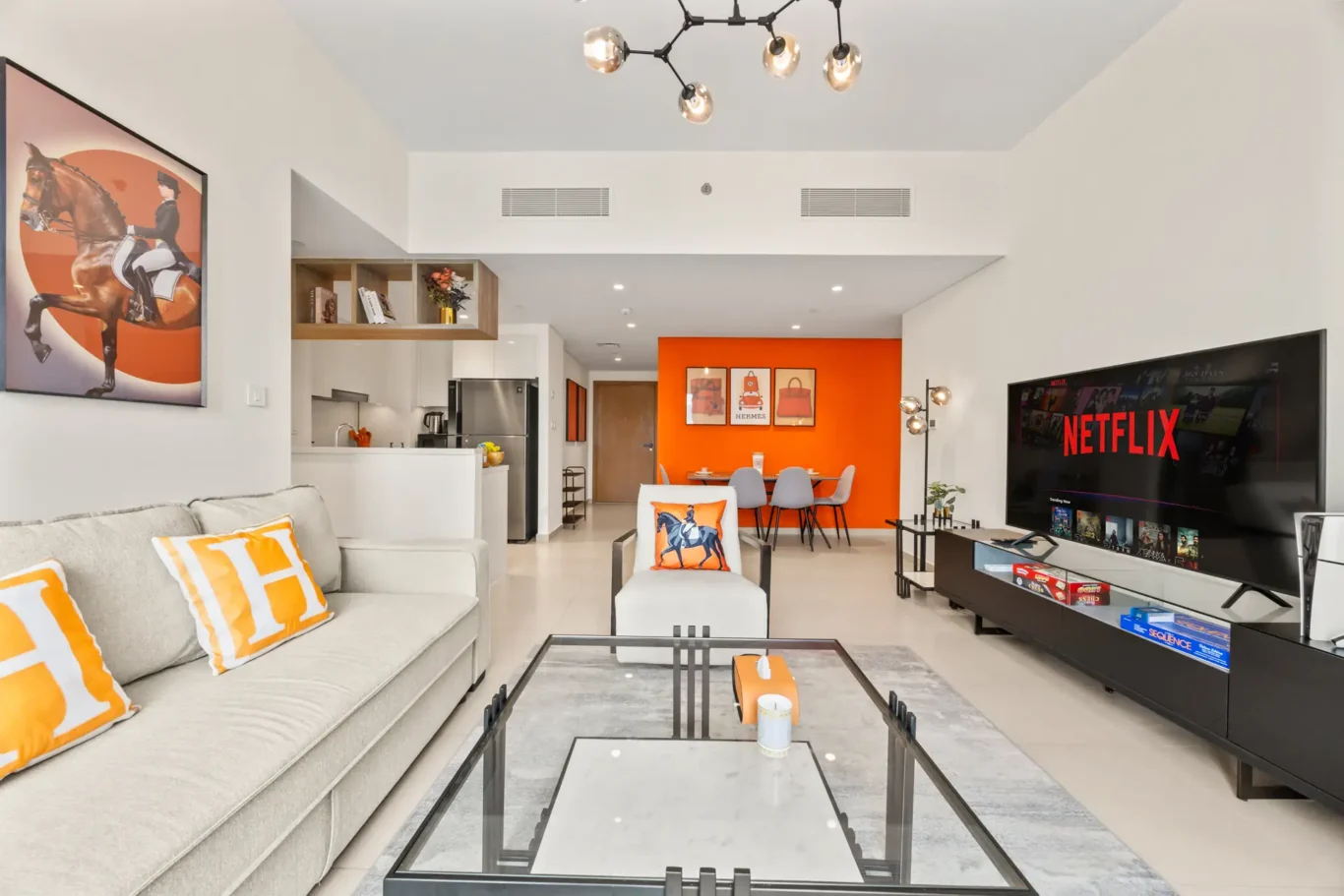 Living room corner with dining table, orange art and open kitchen. Day, twilight and night Airbnb photography by MRPS for Vista Haus Holiday Homes in Downtown Dubai.