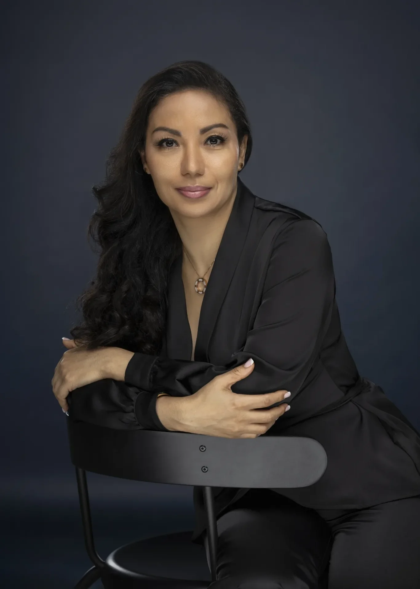 Sandra seated on a black chair in a black outfit, relaxed editorial style portrait. Business profile and LinkedIn portrait photography by MRPS in Dubai.