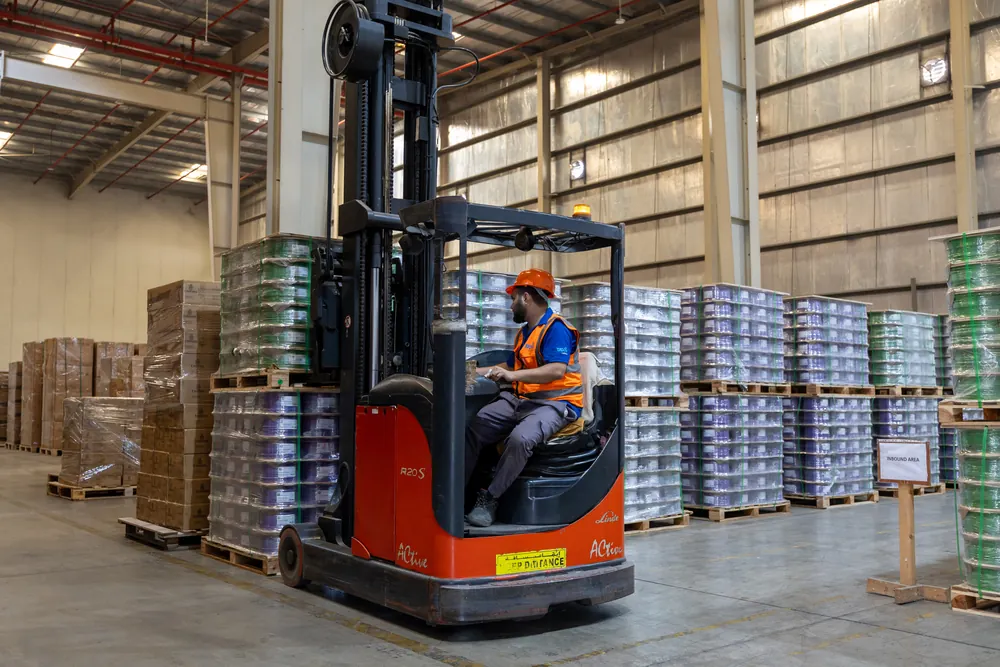 Reach truck operator in safety gear moving between pallets of cable reels inside the Jebel Ali warehouse.