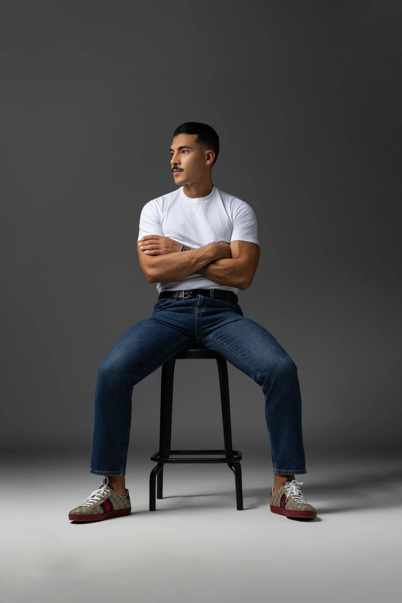 Seated on a stool in a white t-shirt and jeans with arms crossed. Male modeling portfolio photoshoot by MRPS in Dubai, photographed by Nastaran.
