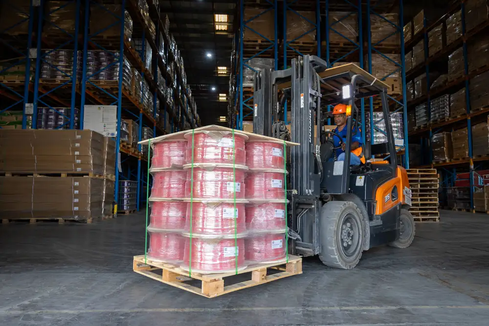 Forklift carrying a pallet of red fire cable reels through the racking aisle of the B3 International warehouse in Jebel Ali.