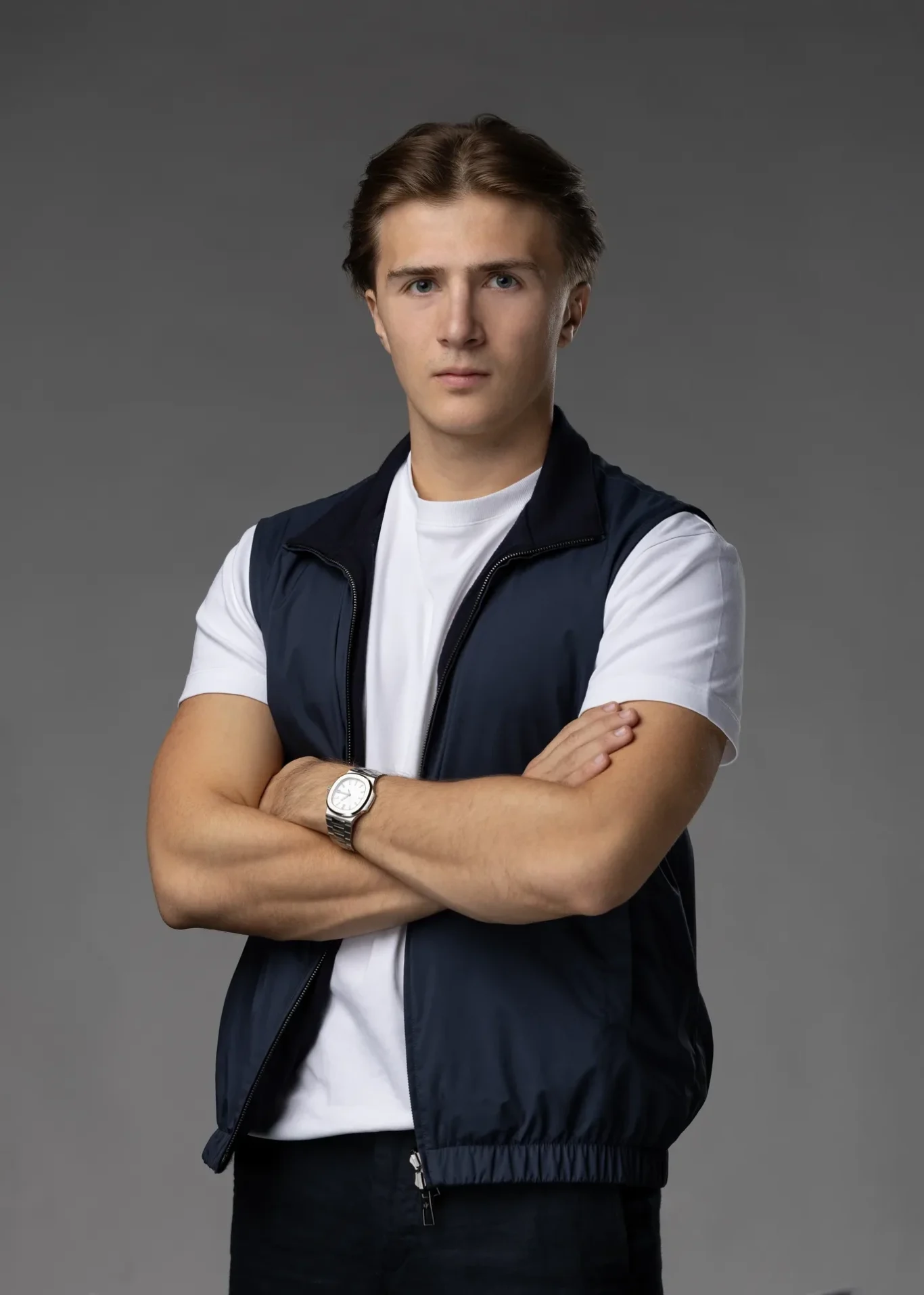 Standing portrait with arms crossed in a navy vest over a white t-shirt, lighter grey backdrop. Editorial business portrait by MRPS in Dubai for a financial magazine feature.
