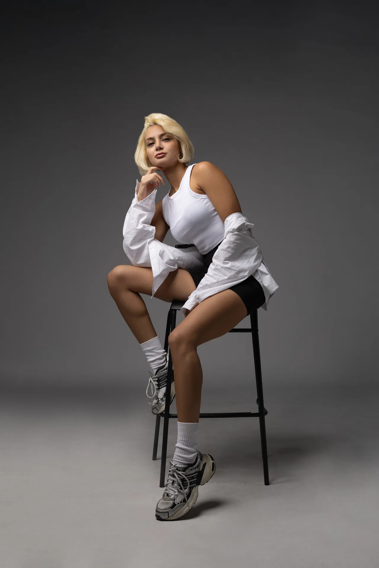 Full-length stool pose of Dr. Aysan Soleymani in a white shirt and sneakers.