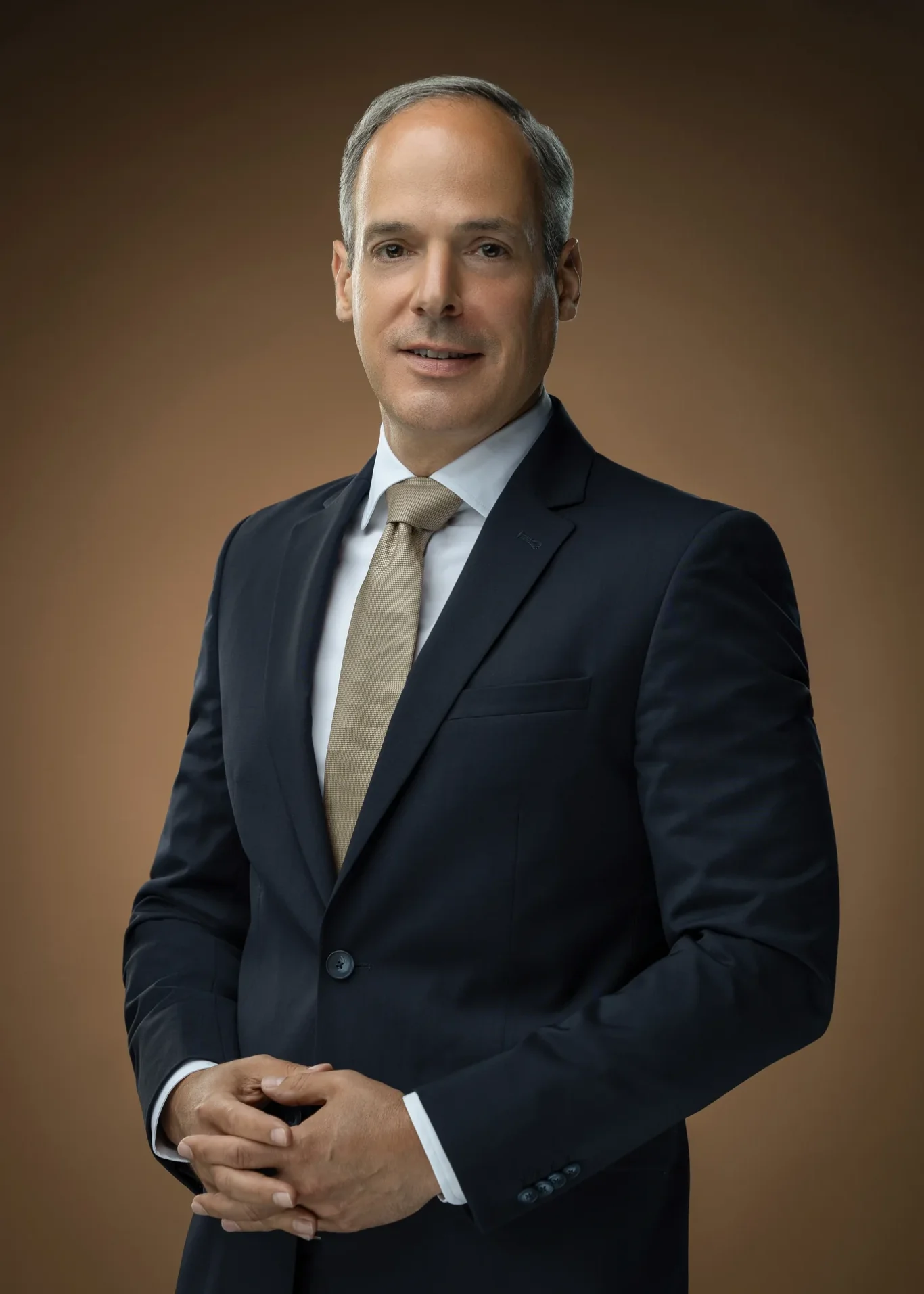 Executive with hands together, gold tie and warm brown backdrop. Corporate business portrait of a Dubai CEO, photographed at the MRPS studio in Business Bay.