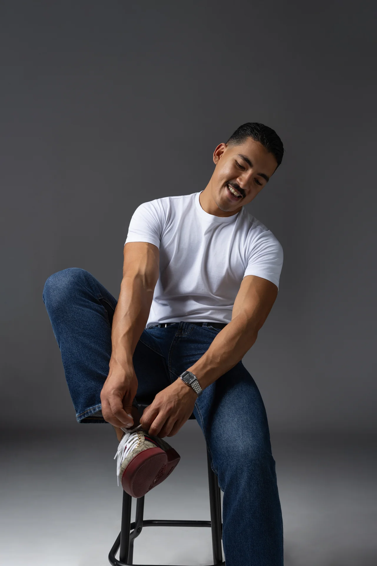 Laughing while seated in a white t-shirt and jeans, tying a sneaker. Male modeling portfolio photoshoot by MRPS in Dubai, photographed by Nastaran.
