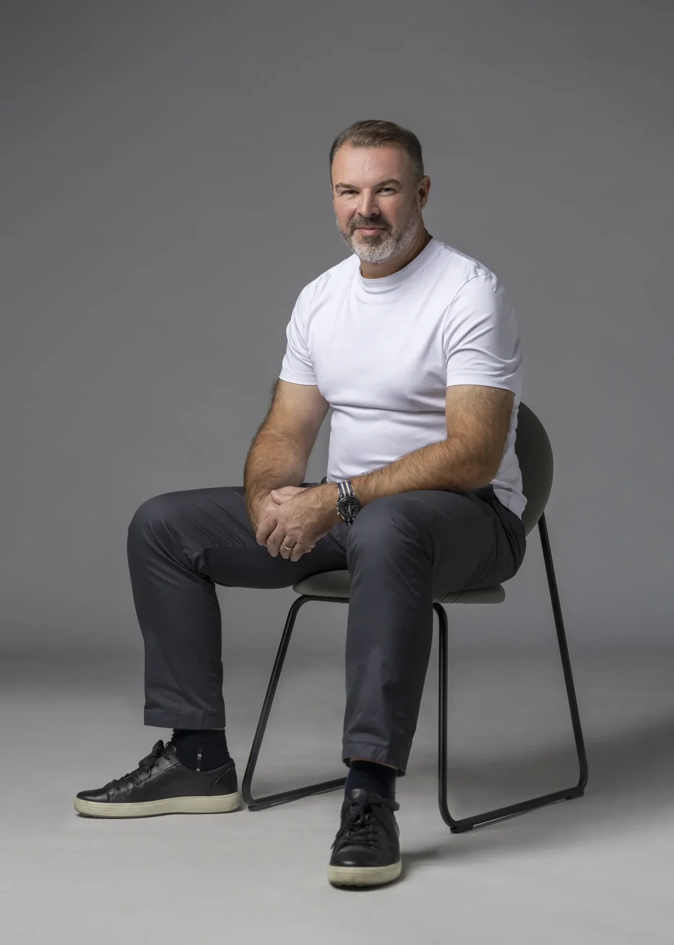 Relaxed seated portrait of Rik Williams in a white t-shirt and dark trousers on a chair. Corporate portrait photography by MRPS in Dubai, photographed by Nastaran.