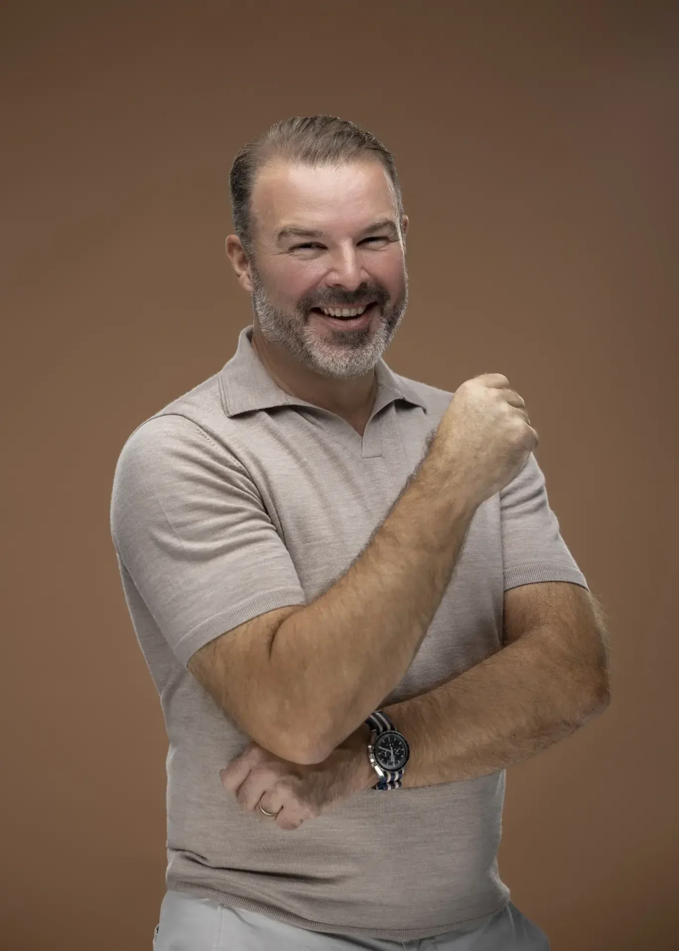 Rik Williams laughing in a beige polo on a warm brown backdrop. Corporate portrait photography by MRPS in Dubai, photographed by Nastaran.