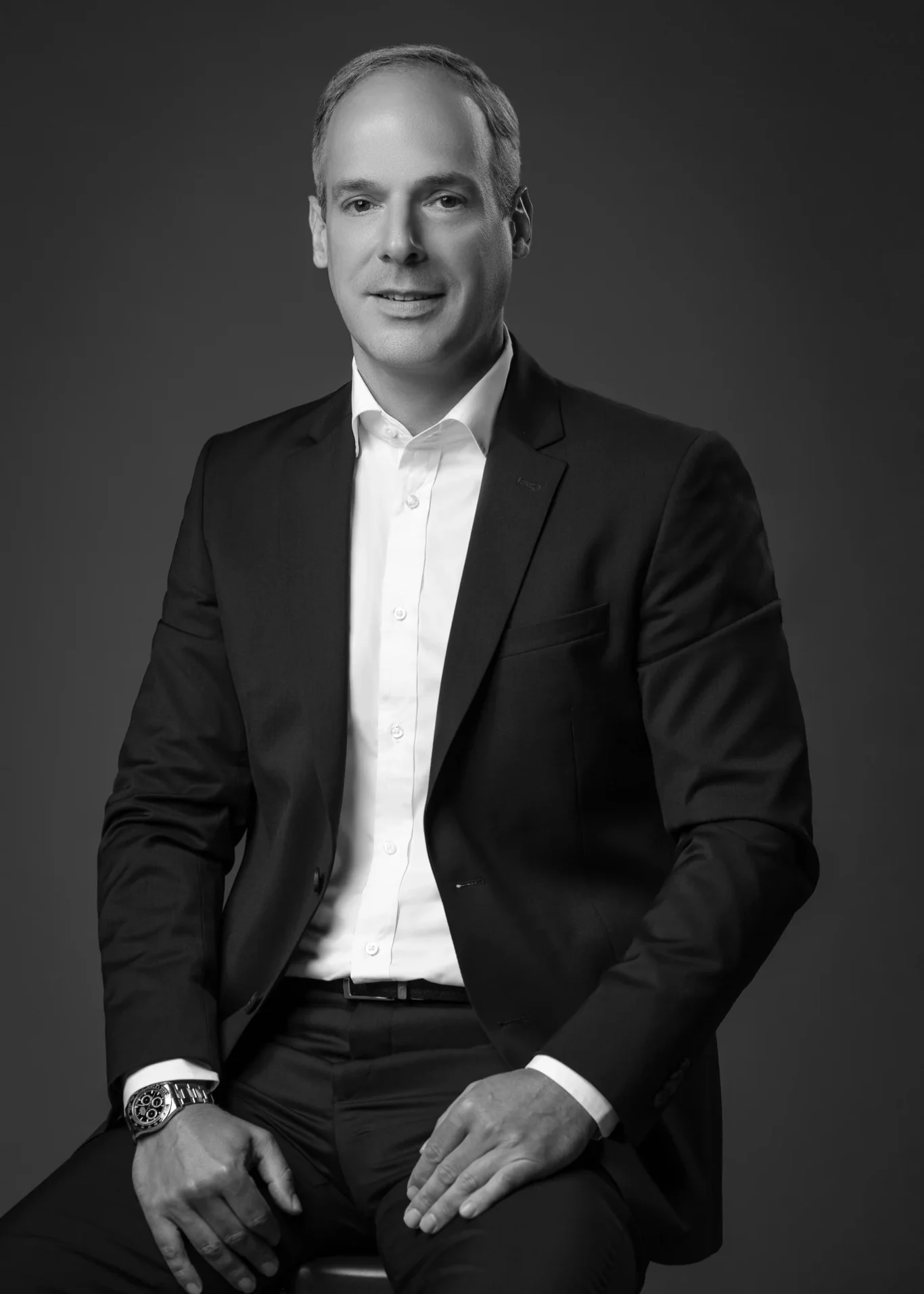 Black and white seated portrait in an open-collar shirt and dark suit. Corporate business portrait of a Dubai CEO, photographed at the MRPS studio in Business Bay.