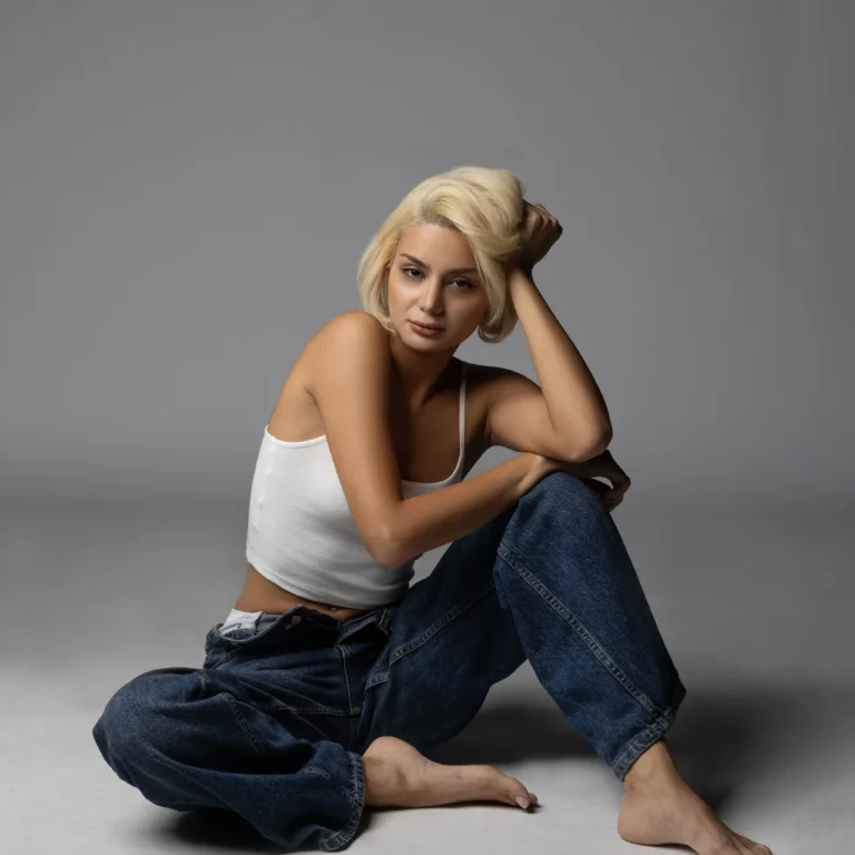 Dr. Aysan Soleymani seated on the studio floor in wide denim jeans.