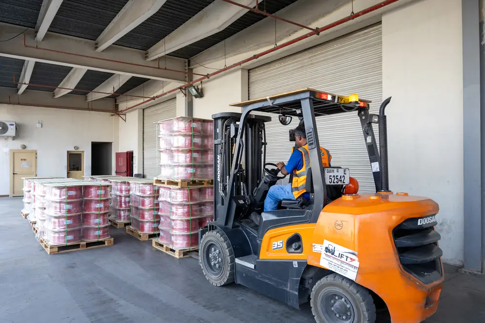 Orange forklift moving pallets of red cable reels at the loading bay of the Jebel Ali distribution warehouse.
