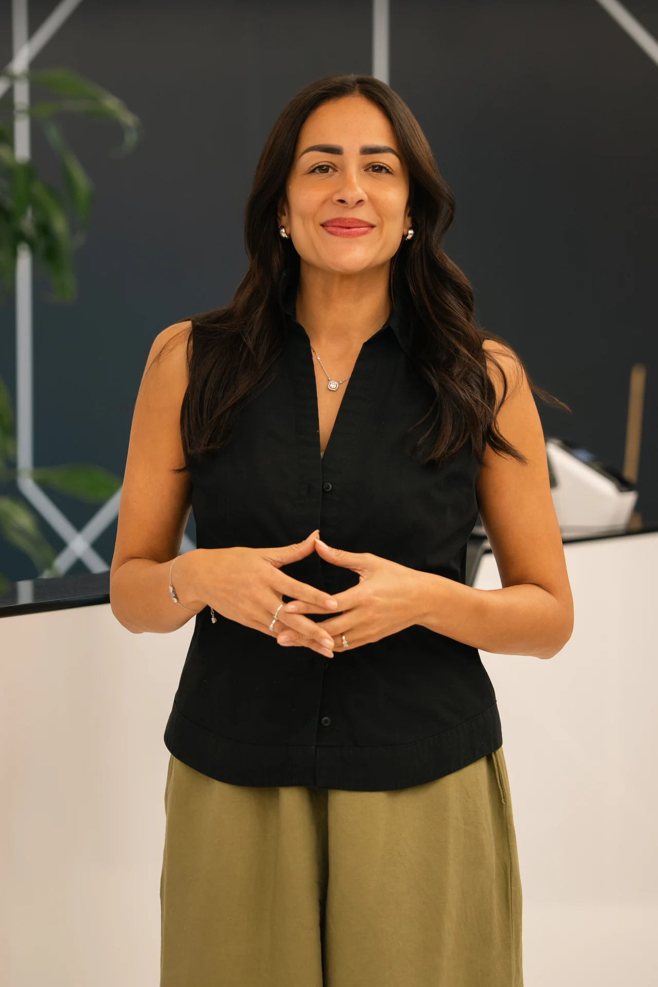 Standing portrait with hands together against a dark feature wall. On-site corporate headshot at the Nutanix office in Dubai.