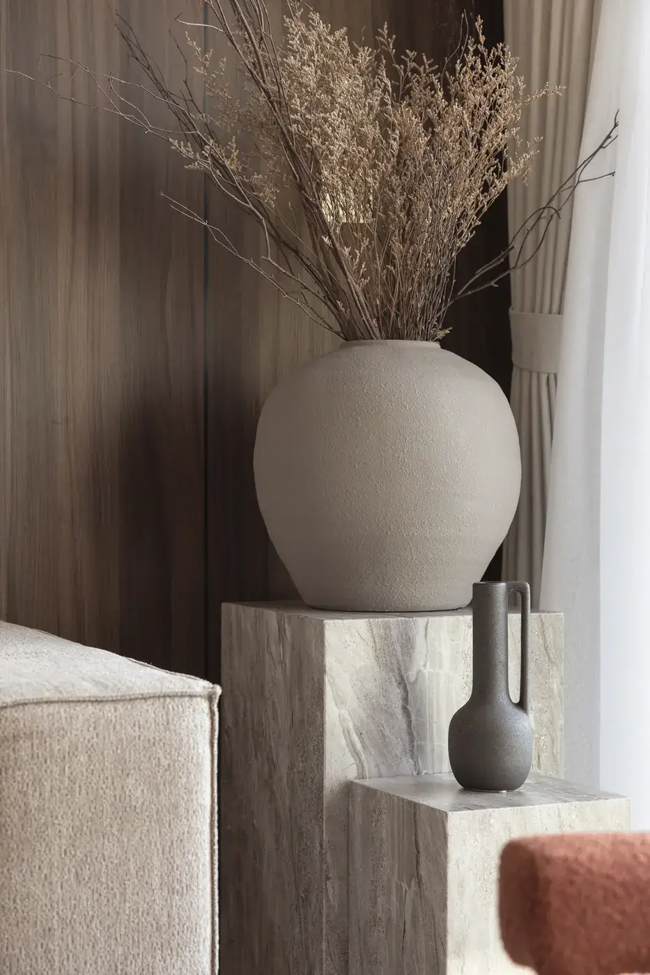 Grey stone vase on a travertine plinth beside the sofa. Interior design photography for Aziza Home by MRPS in Dubai.