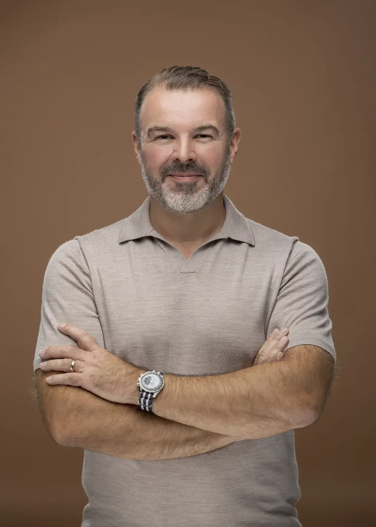Rik Williams in a beige polo with arms crossed on a warm brown backdrop. Corporate portrait photography by MRPS in Dubai, photographed by Nastaran.