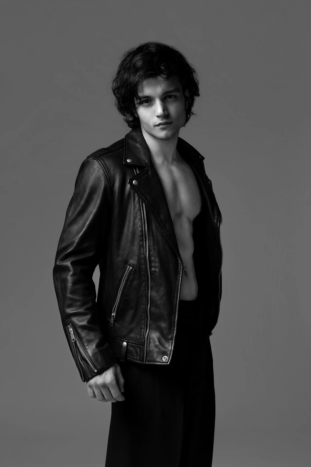 Black and white portrait of Arsh standing in an open leather jacket, hands in his pockets.