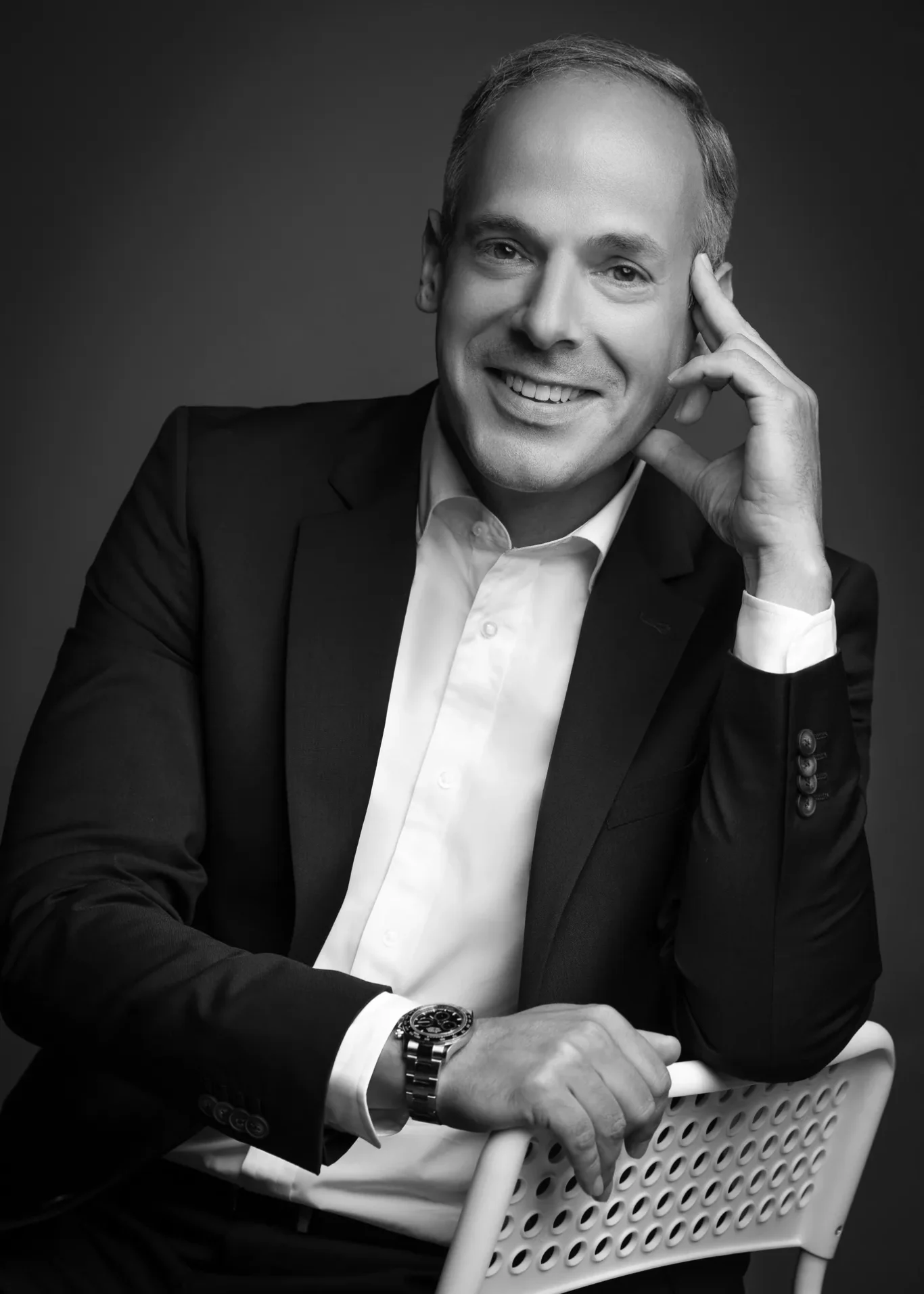 Black and white portrait smiling, leaning on a chair with hand at temple. Corporate business portrait of a Dubai CEO, photographed at the MRPS studio in Business Bay.