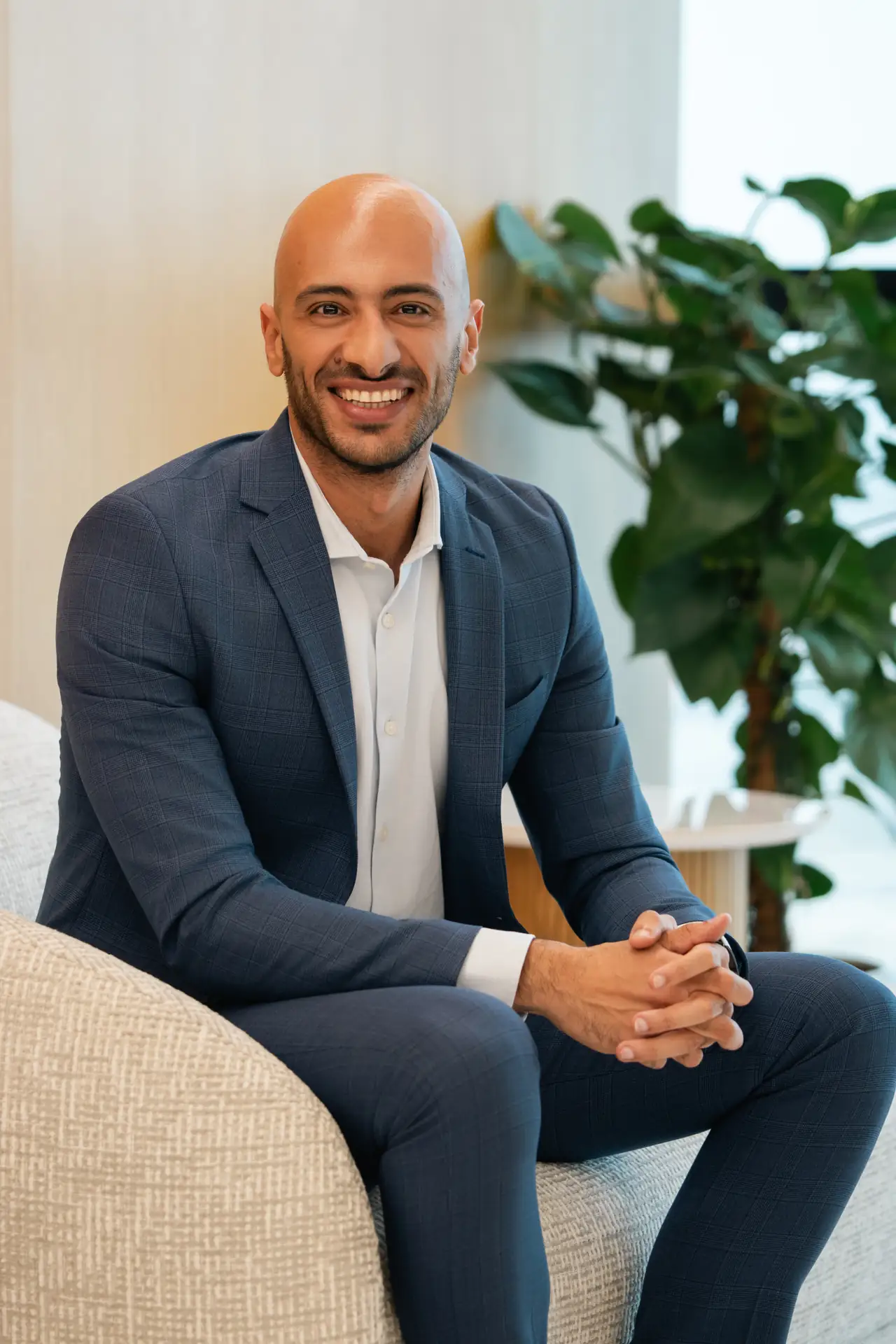 Seated portrait in a navy suit beside office plants. On-site corporate headshot at the Nutanix office in Dubai.