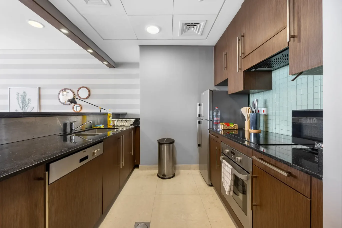 Fitted kitchen with dark worktops and wood cabinets in a Your Stay Apartments one-bedroom at Burj Daman, DIFC, Dubai.