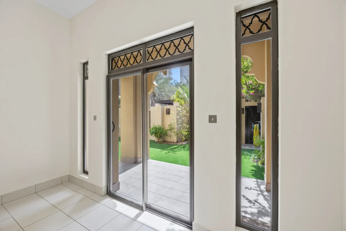 Sliding glass doors with Arabian lattice detail opening to the garden in an unfurnished two-bedroom garden apartment in Old Town, Downtown Dubai, photographed for ELITE Property Brokerage.