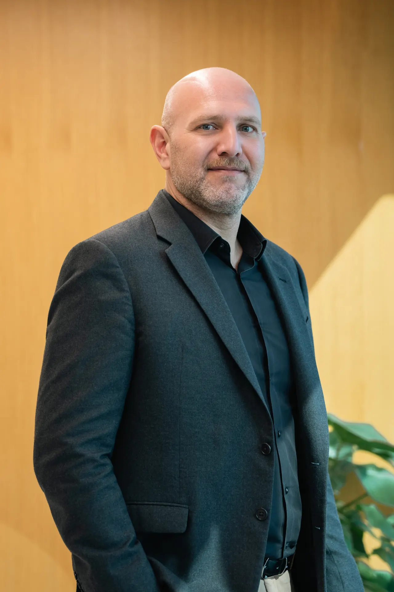 Standing portrait in a dark blazer against wood panelling. On-site corporate headshot at the Nutanix office in Dubai.