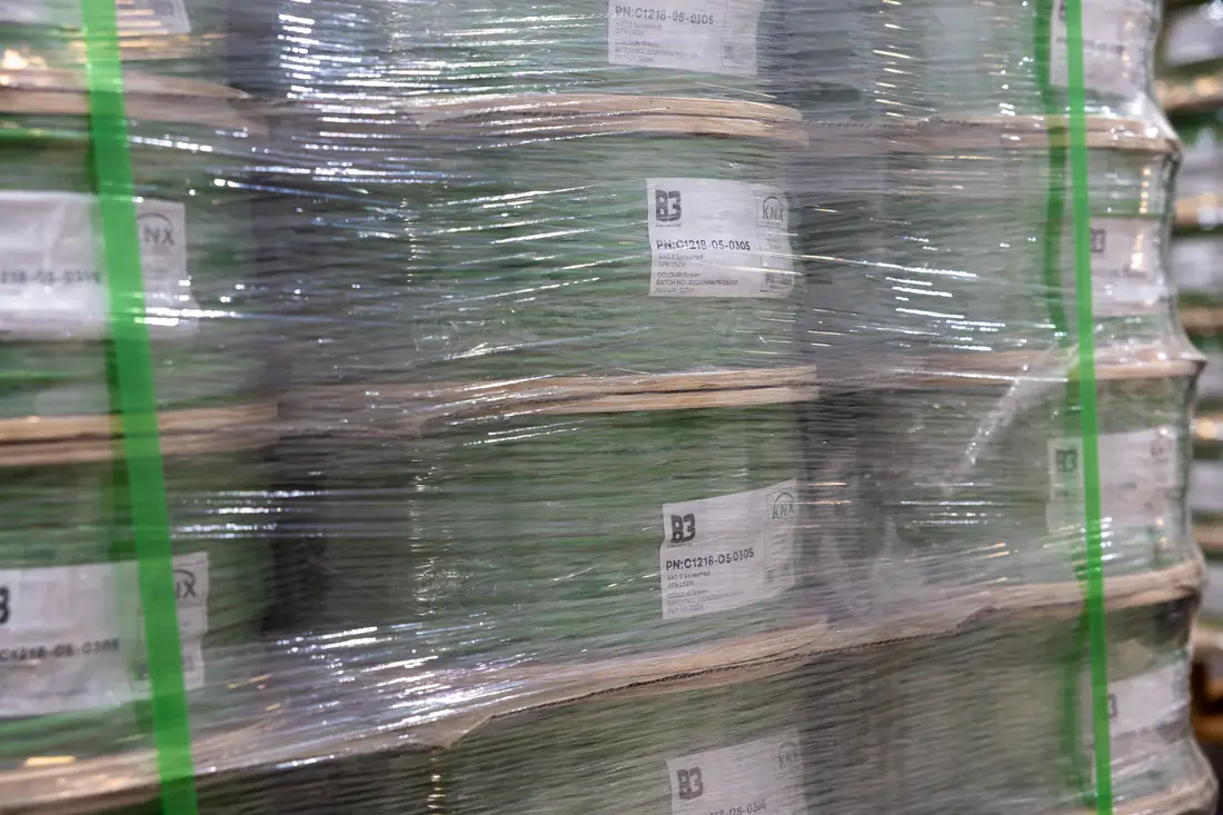 Detail of stretch-wrapped green cable reels with B3 product labels on a warehouse pallet.