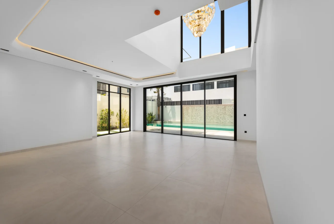 Double-height living area with a chandelier and pool view, unfurnished five-bedroom villa in Al Furjan, Dubai.