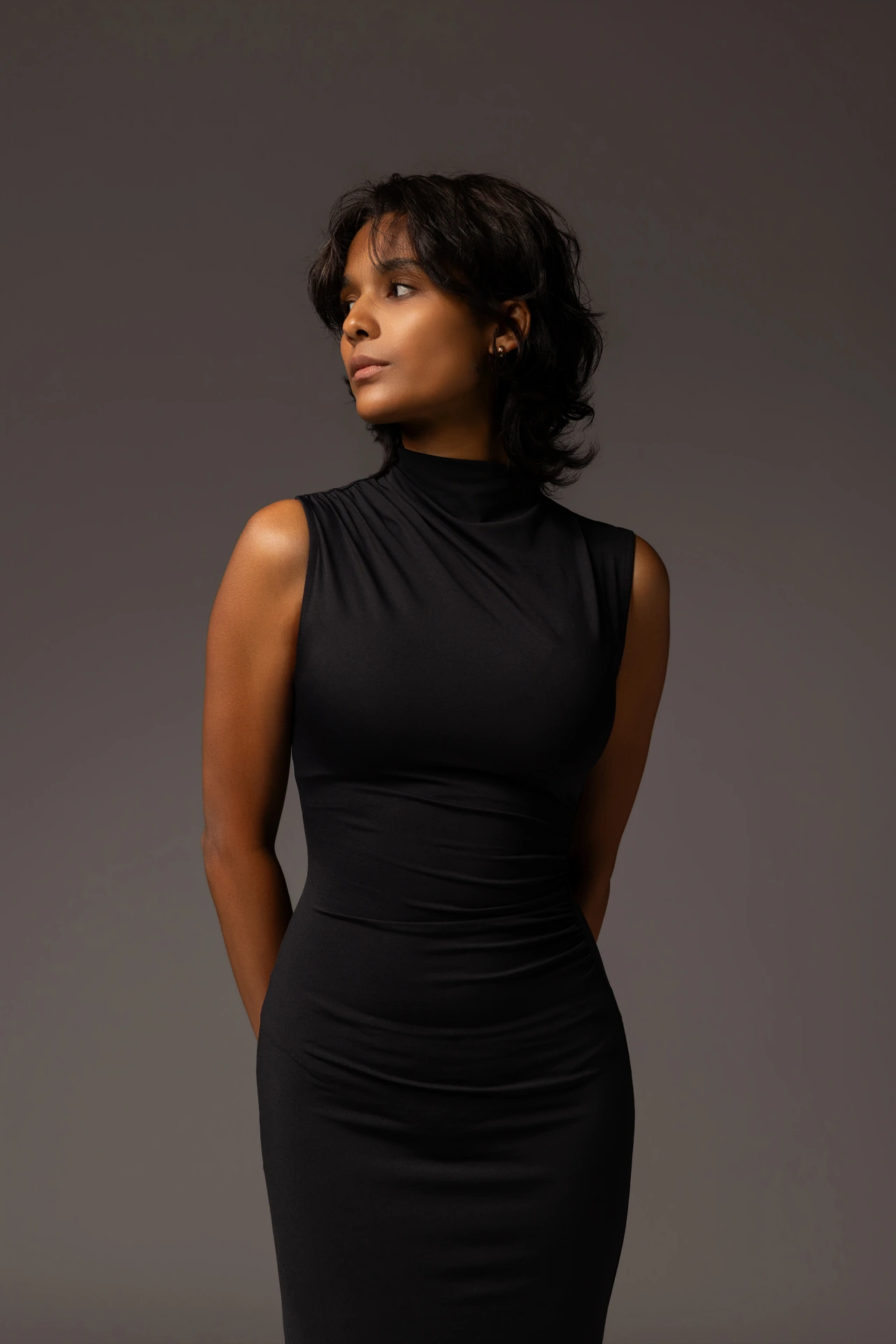 Three-quarter shot of Mia in a black sleeveless dress looking away from the camera.