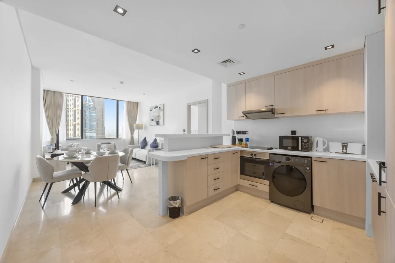 Open kitchen with dining table and city view in a Your Stay Apartments one-bedroom at Sky Gardens, DIFC, Dubai.